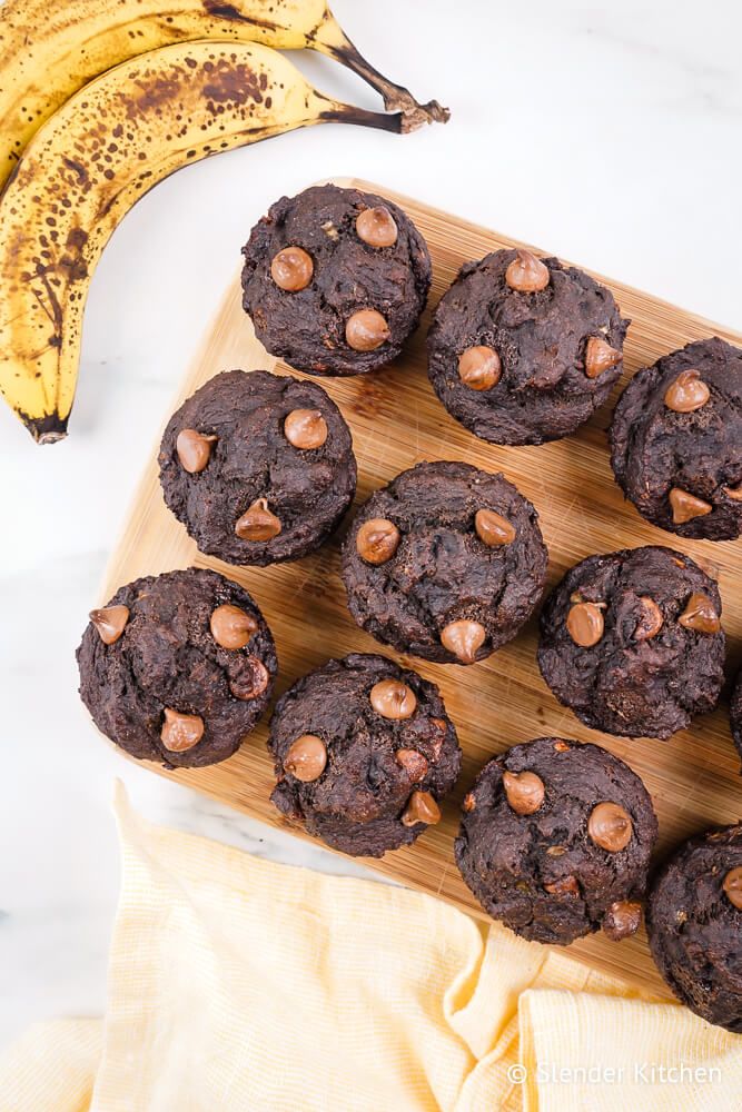 Banana chocolate muffins with chocolate chips on a wooden board with bananas.