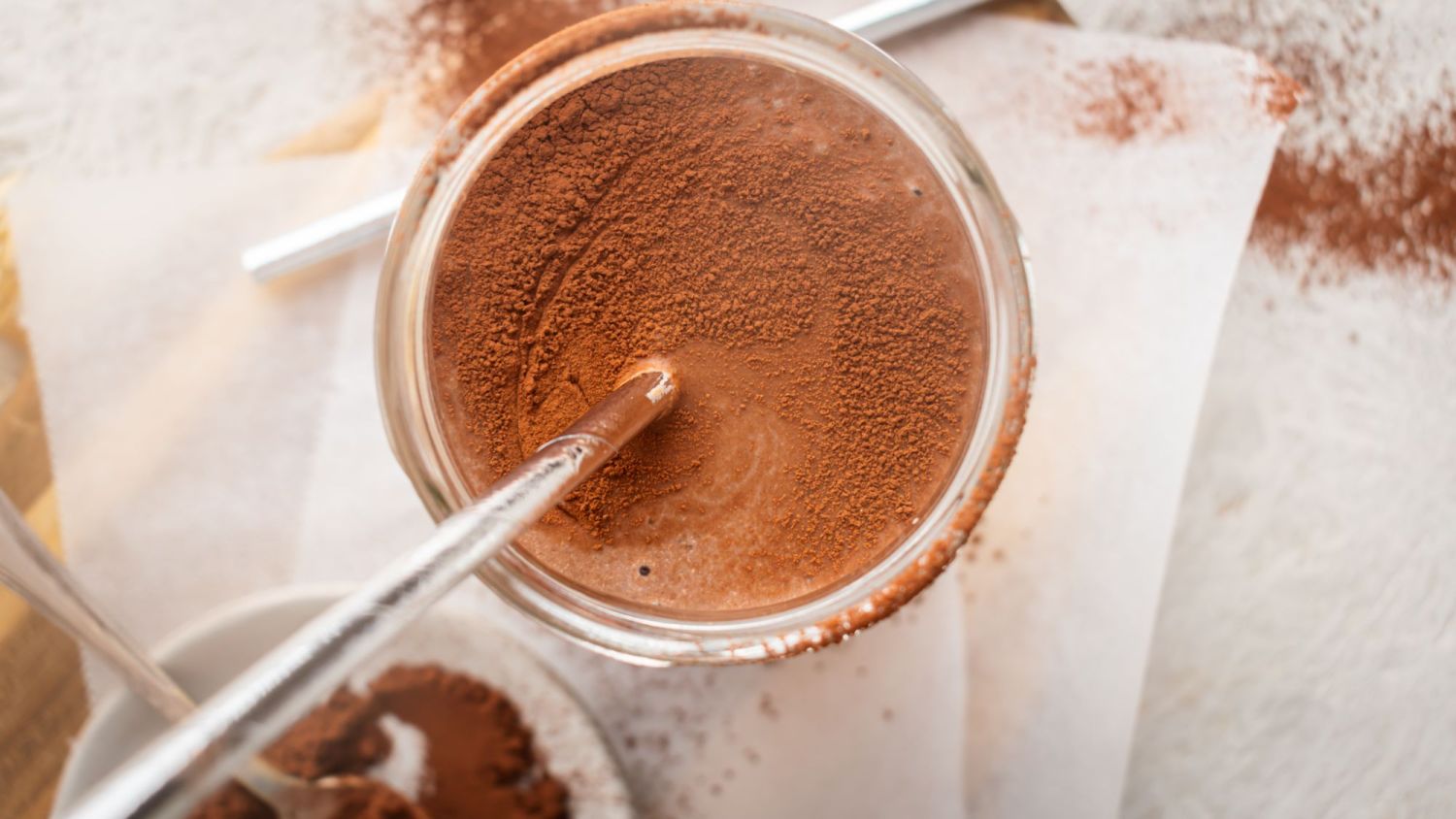 Protein chocolate shake with almond milk, banana, and tofu blended in a glass with cocoa powder dusted on top.