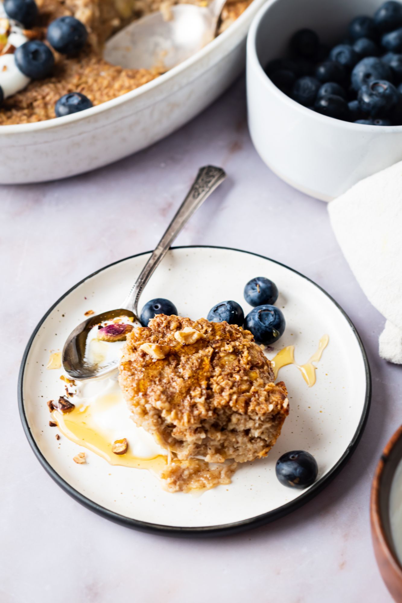 Baked cinnamon oatmeal served on a plate with fresh blueberries, yogurt, and honey.