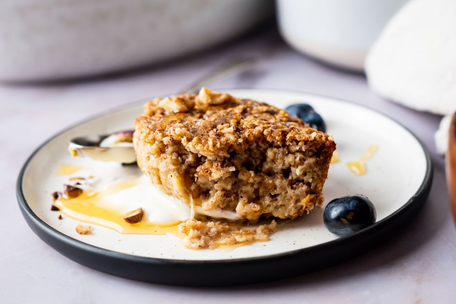 Baked oatmeal with cinnamon cut into a square and served with honey and blueberries.