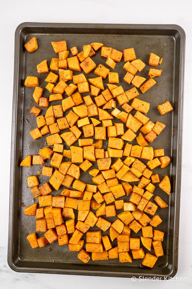 Roasted butternut squash on a baking sheet with cinnamon and nutmeg.