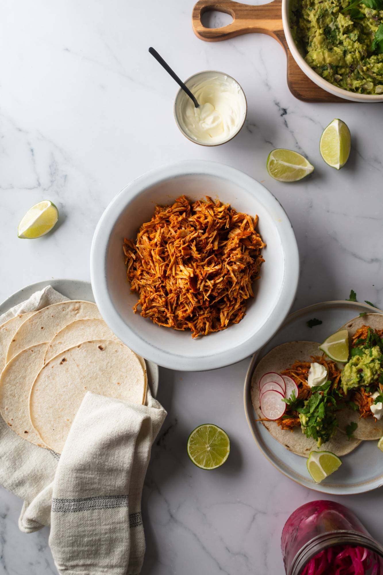 Mexican cochinita pibil shredded in a bowl with tacos and guacamole on the side.