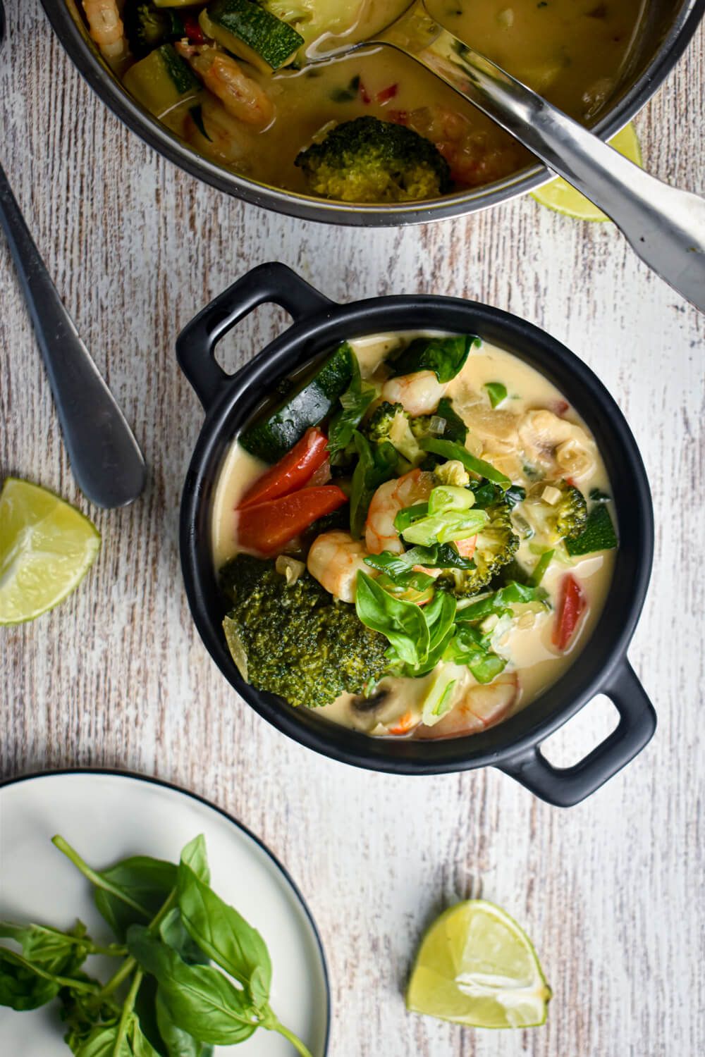 Coconut shrimp with curry paste and fresh vegetables in a bowl with fresh basil, green onions, and lime juice.