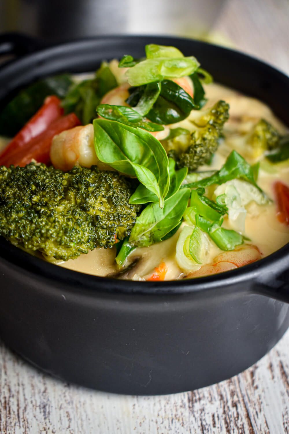 Curry shrimp with coconut milk, fresh vegetables, Thai green curry paste, and basil in a black dish with fresh limes.