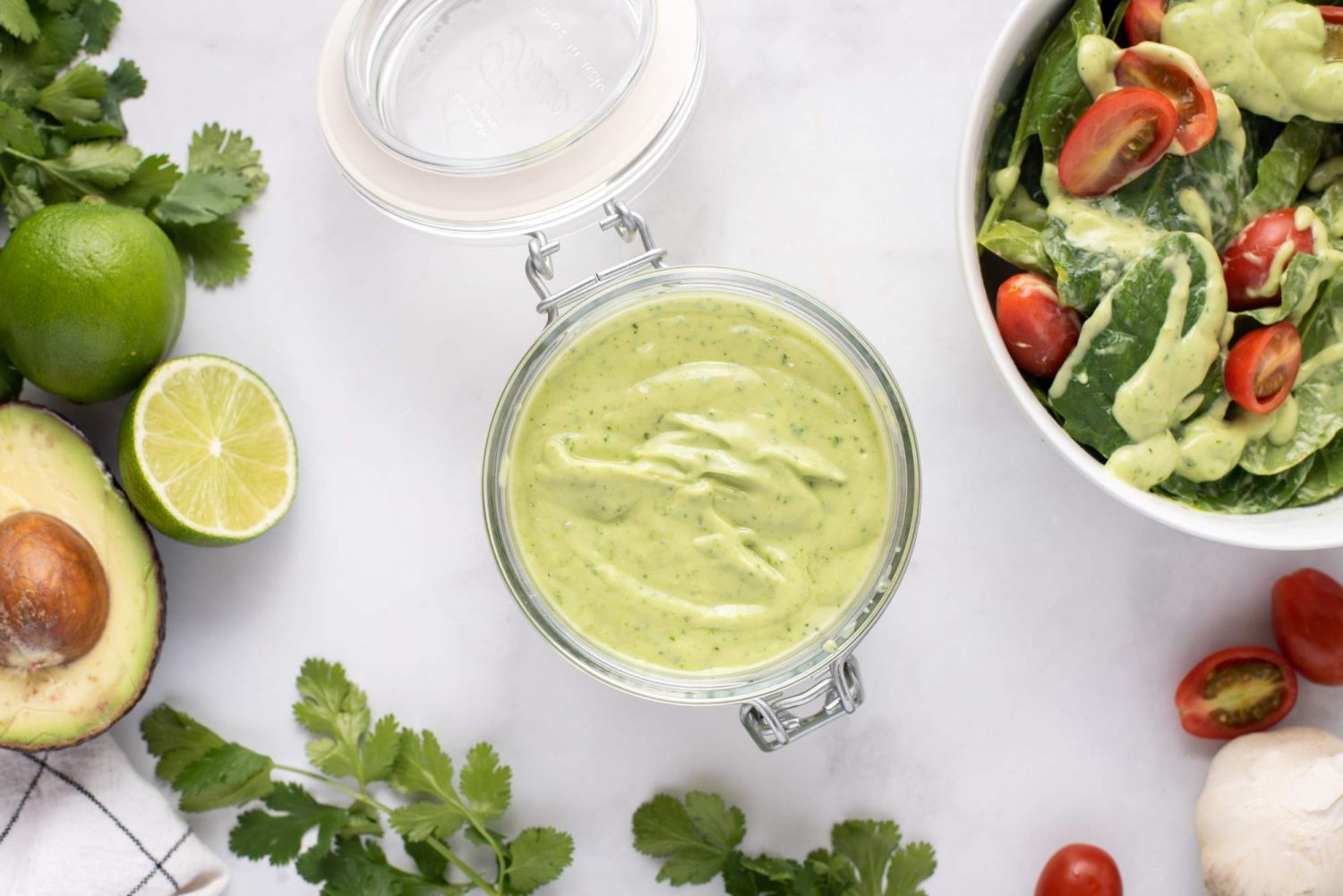 Avocado salad dressing with cilantro, lime juice, and yogurt in a glass jar with fresh vegetables on the side.