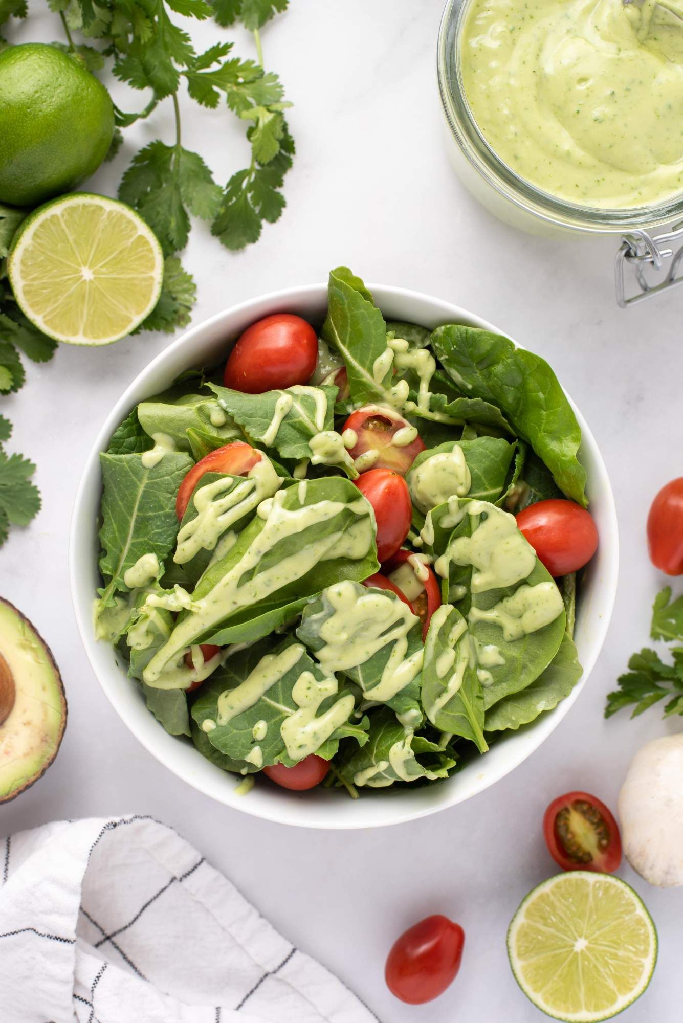 Green salad with tomatoes drizzled with creamy avocado dressing with cilantro and avocado on the side.