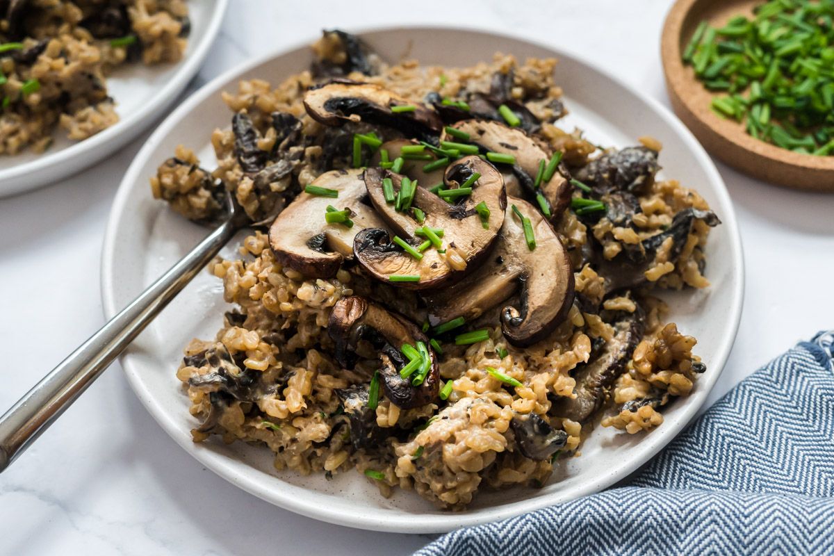 Mushroom brown rice on a plate with tender cooked mushrooms on a bed of creamy rice with chives.