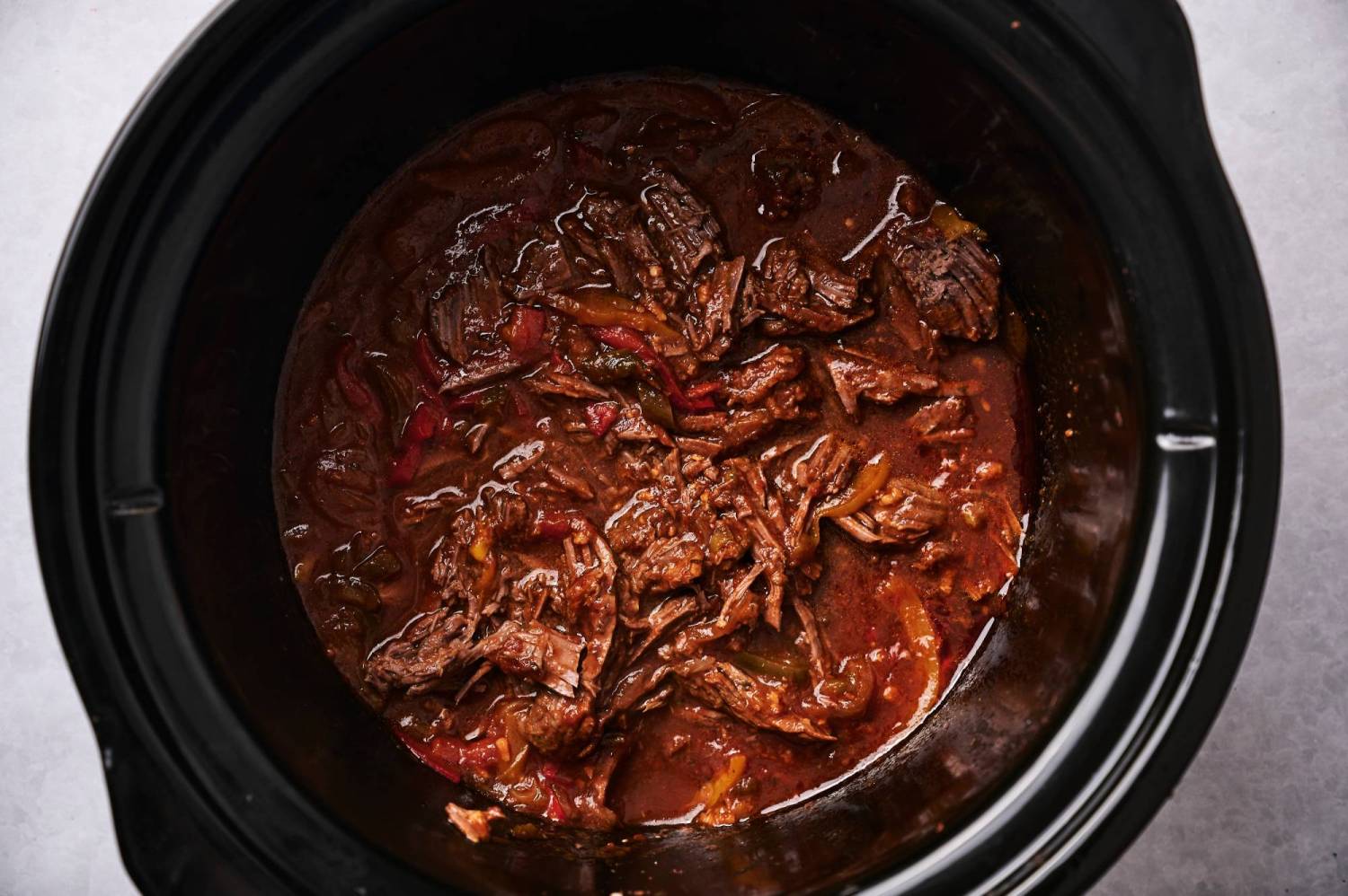 Crockpot steak fajitas in a slow cooker with shredded beef, peppers, onions, and tomato sauce.