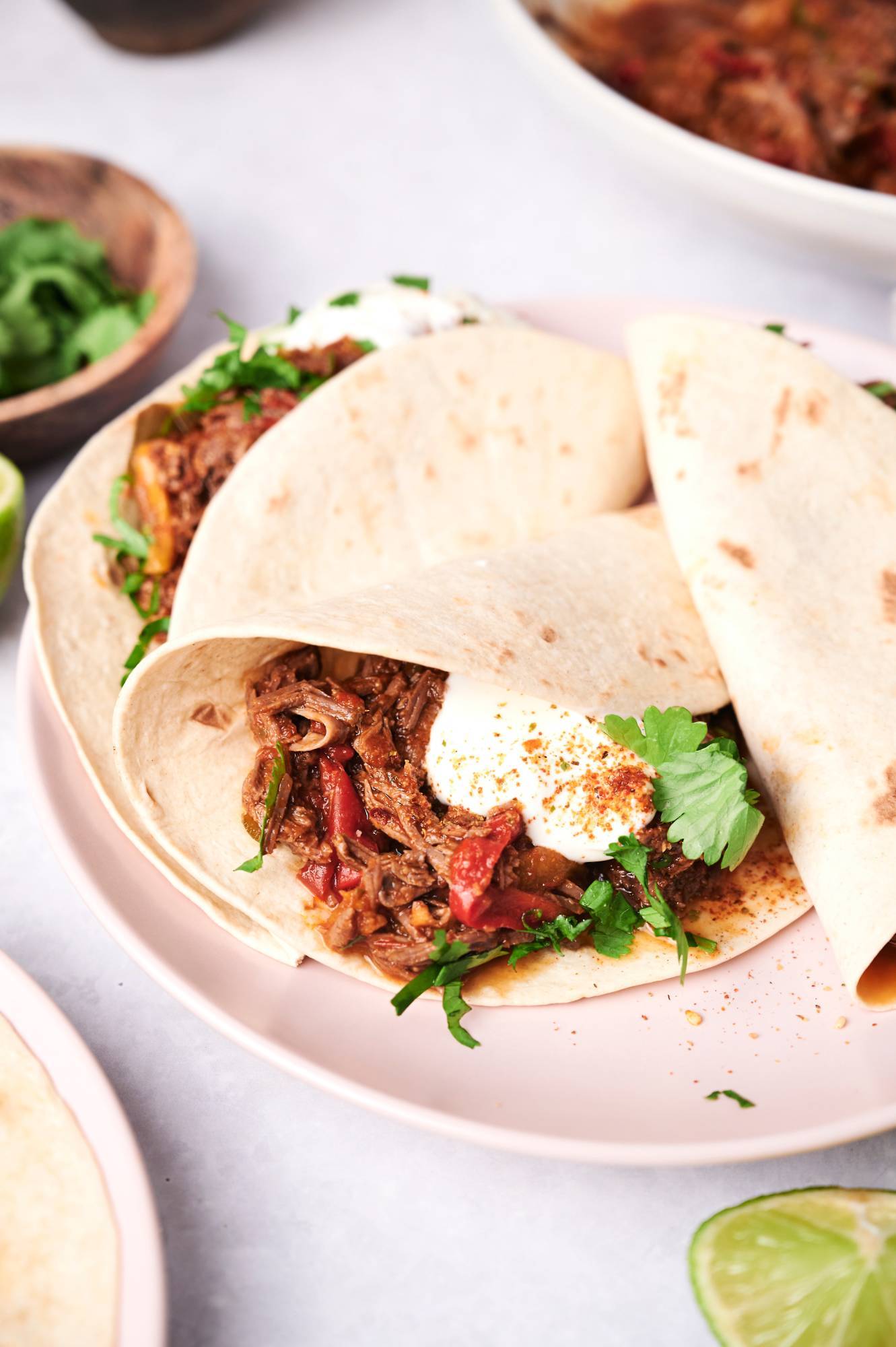Beef fajitas made in the slow cooker served on a flour tortilla with cilantro and sour cream.