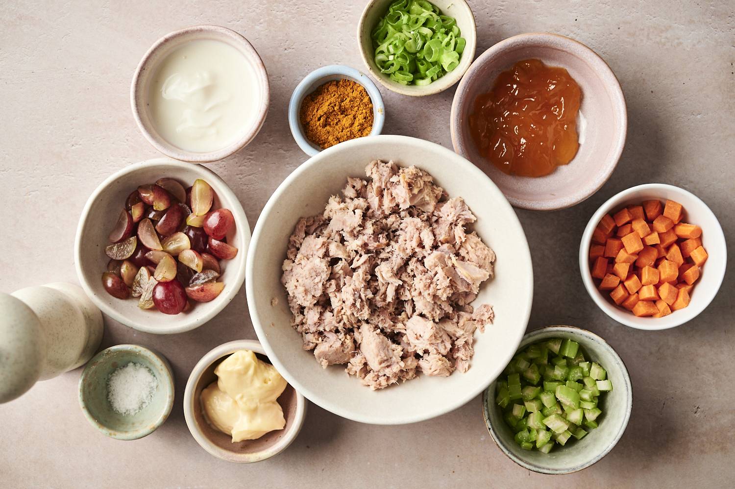 "Tuna salad ingredients are arranged in bowls: flakes of tuna, diced, celery, half grapes, thinly sliced ​​green onion, mayonnaise, Greek yogurt, chutney, chutney, curry powder and salt