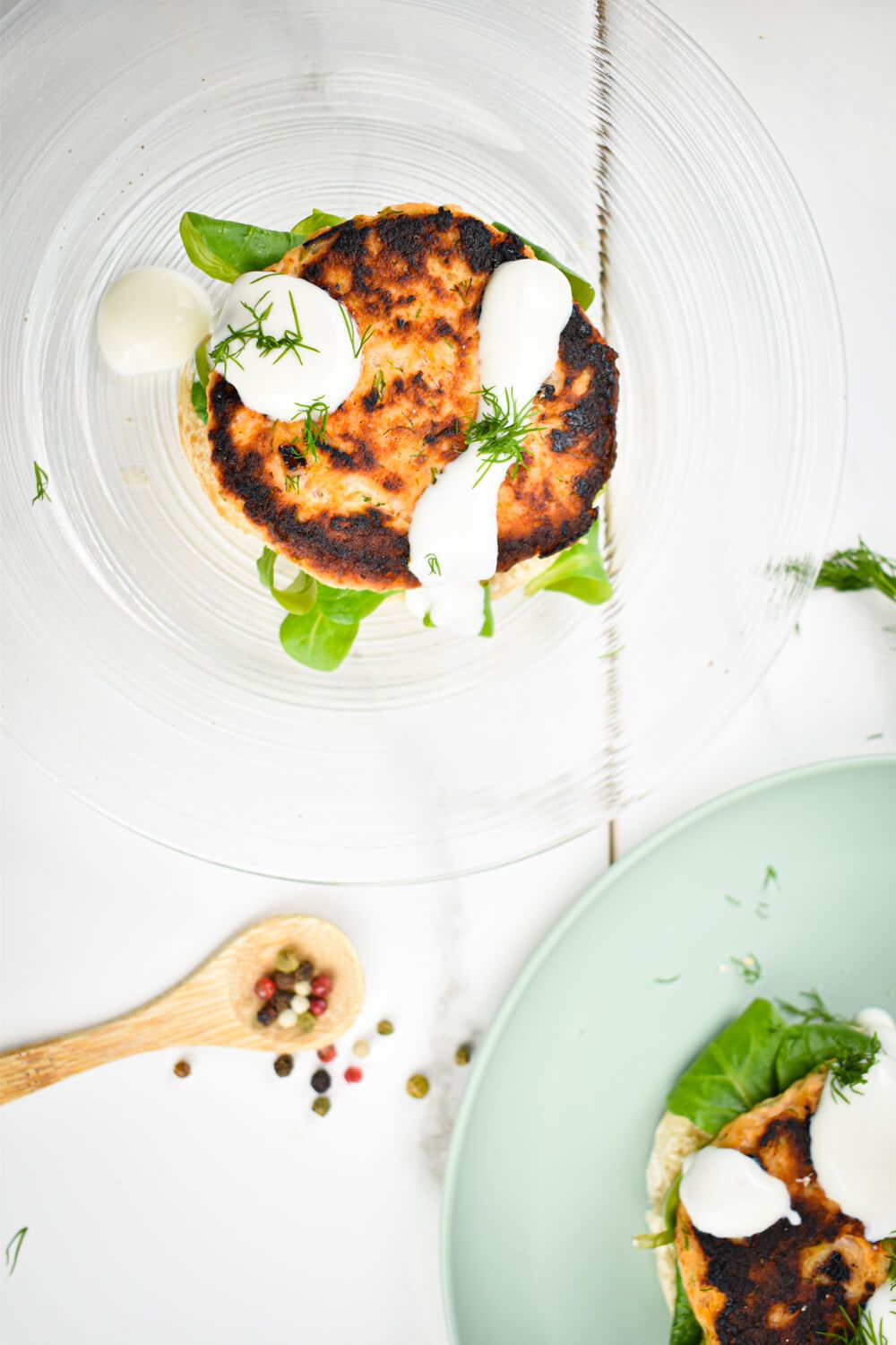 Burgers made with salmon and fill on a plate with lettuce, yogurt sauce, and whole wheat buns.