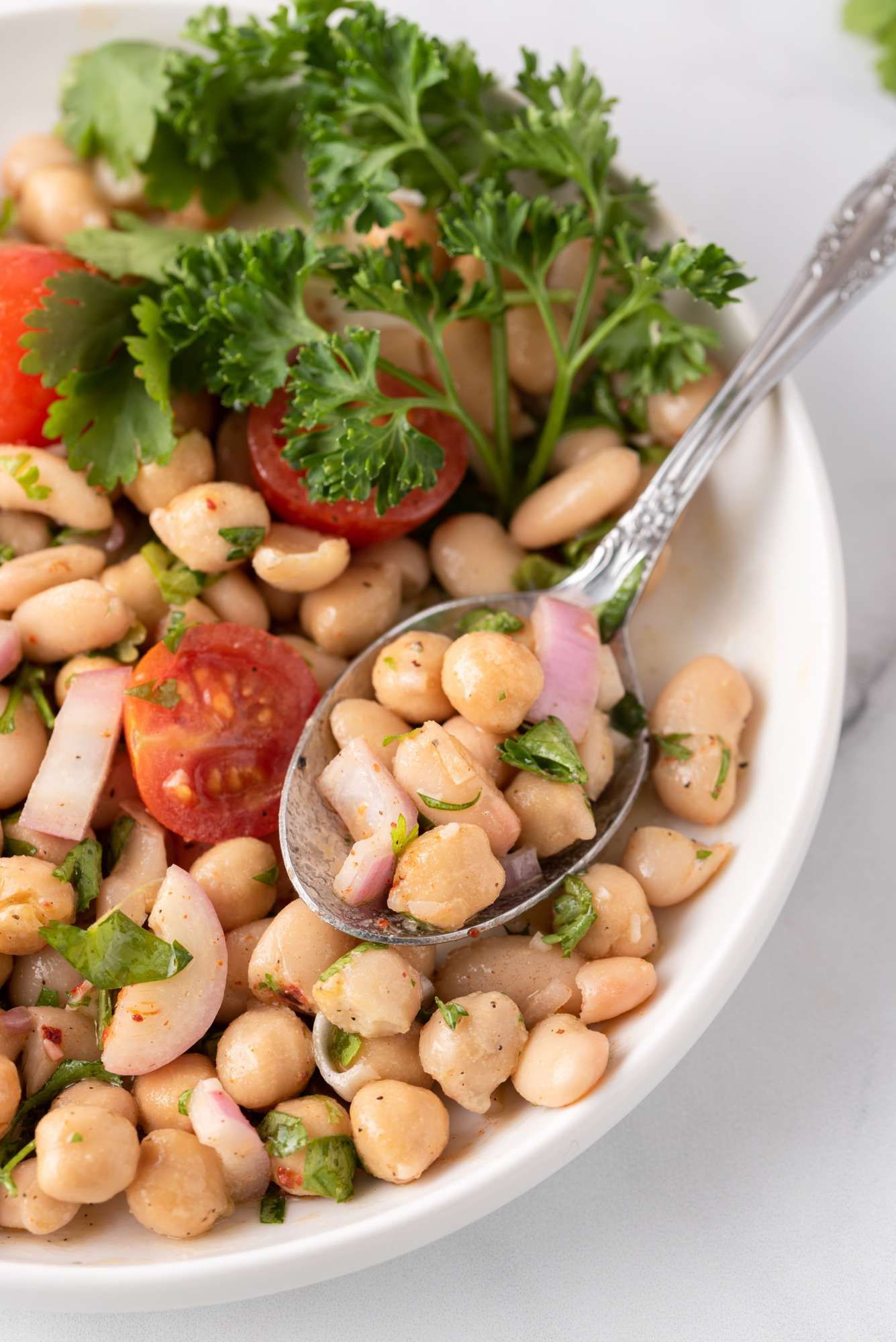 Chickpea and white bean salad with shallots, fresh herbs, and tomatoes in a bowl.