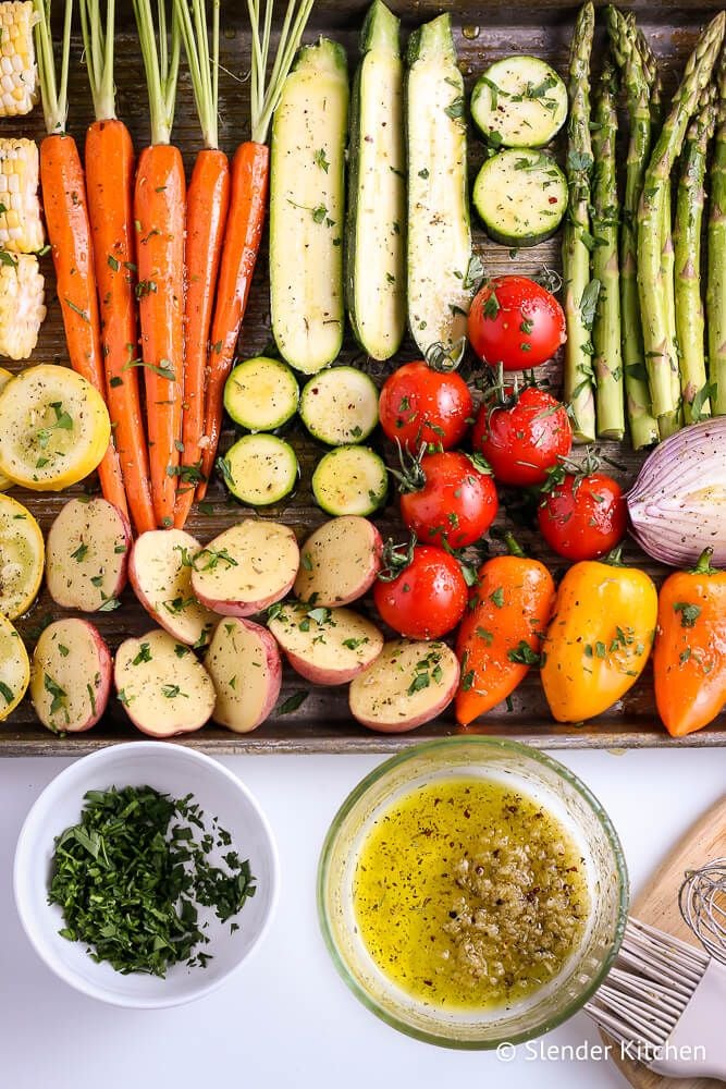 Various vegetables being prepped for grilling including carrots, zucchini, corn, asparagus, tomatoes, bell peppers, and red onions.