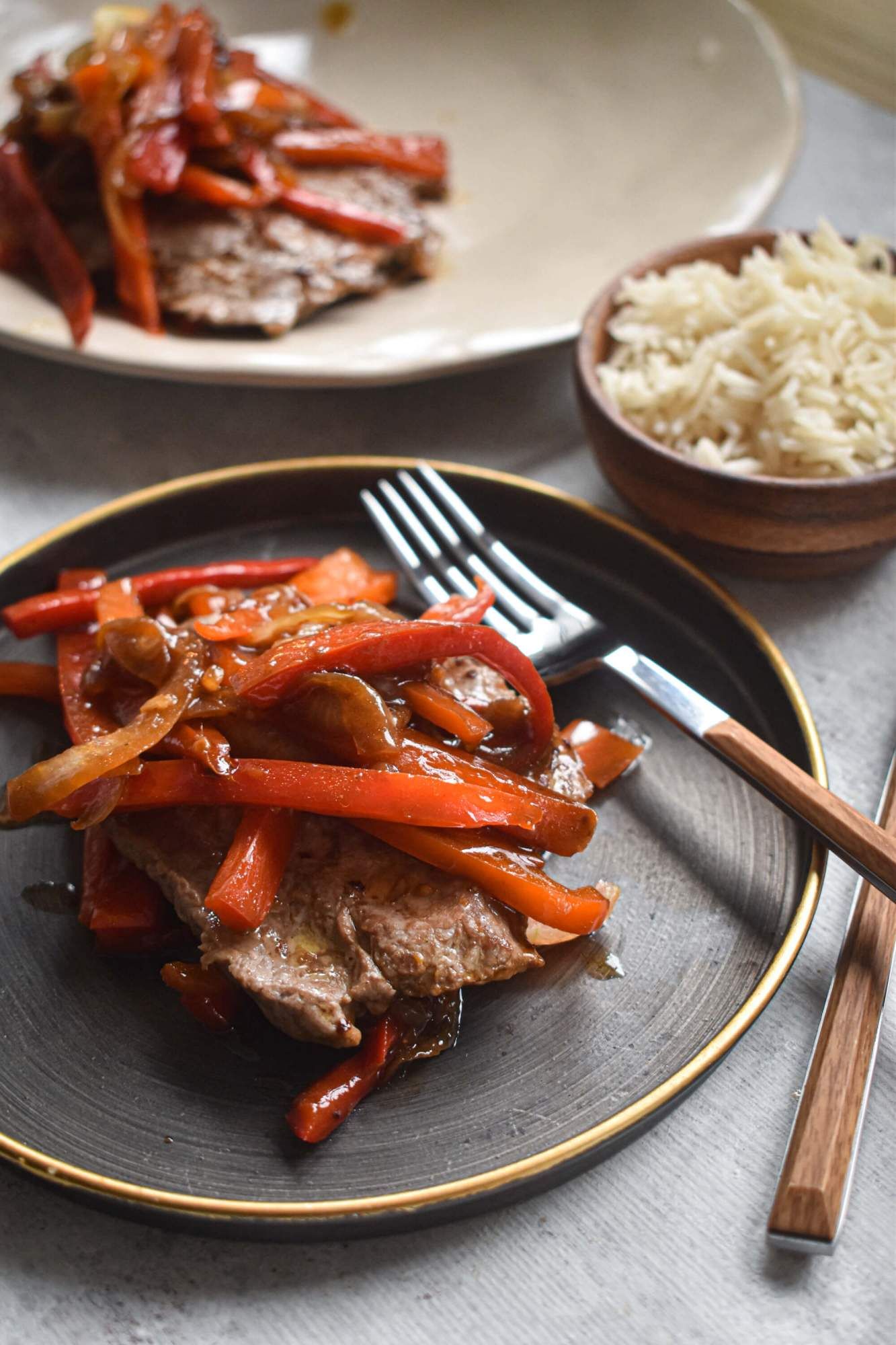 Pepper steak stir fry with a thin steak piled with peppers and onions on a plate with a fork and knife.