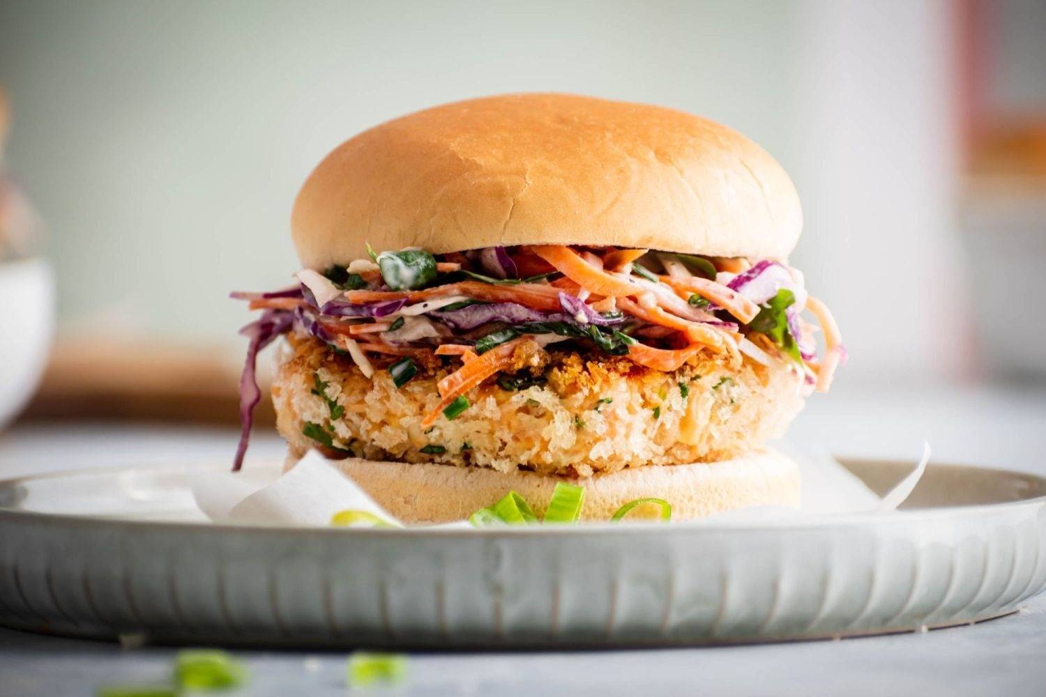 Crispy salmon burger with cabbage and carrot coleslaw on a white burger bun.