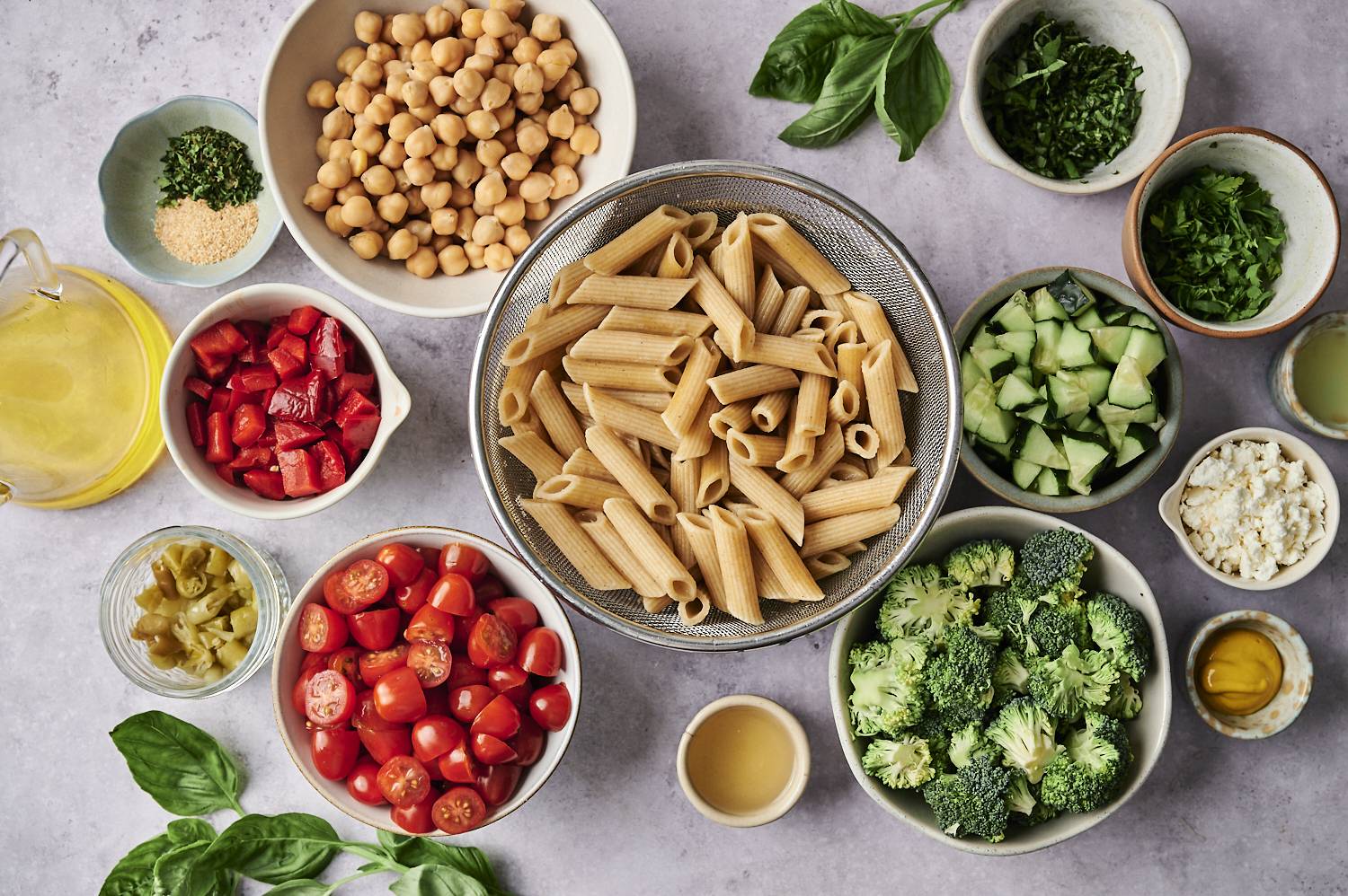 An assortment of ingredients for a healthy meal, including whole grain pasta, chickpeas, tomatoes, broccoli, and various vegetables.