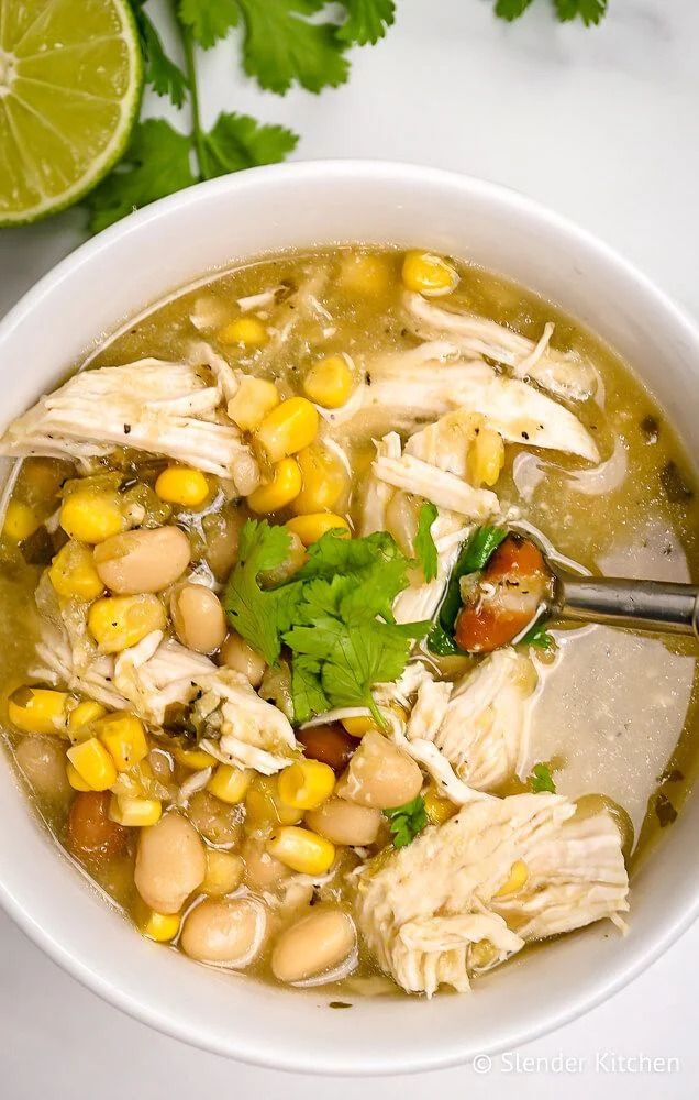 Healthy chicken chili with chicken breast, beans, cilantro, and lime in a white bowl.