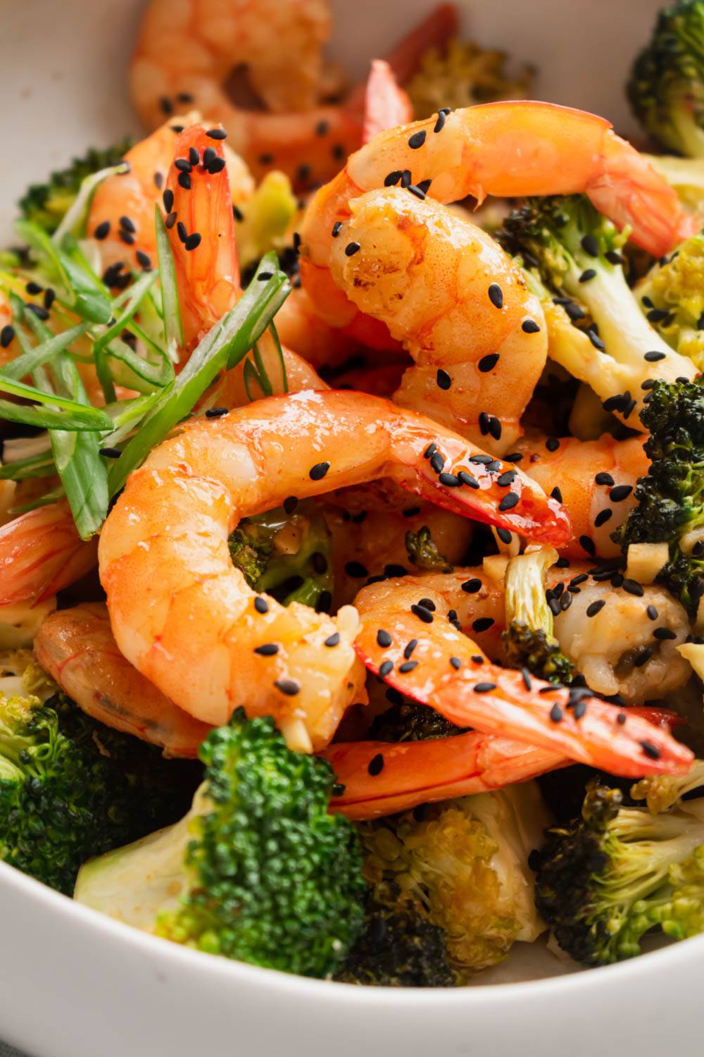 A close-up of firecracker shrimp and broccoli, garnished with sliced scallions and sesame seeds.
