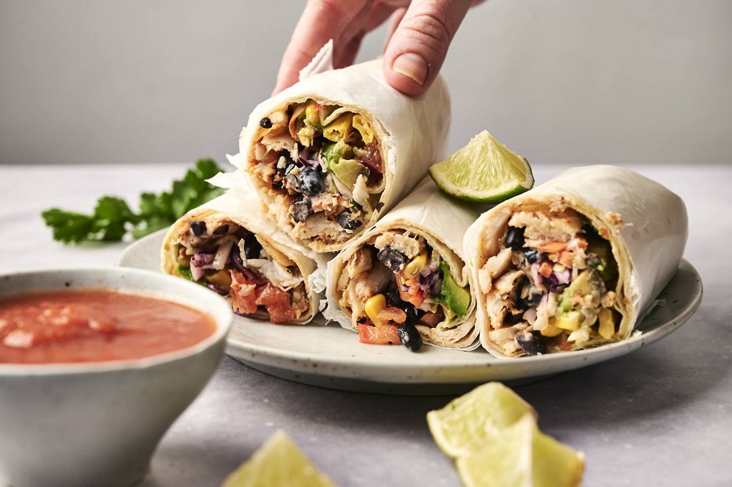 Three delicious burritos, filled with chicken, black beans, and fresh vegetables, served with a lime wedge and dipping sauce.
