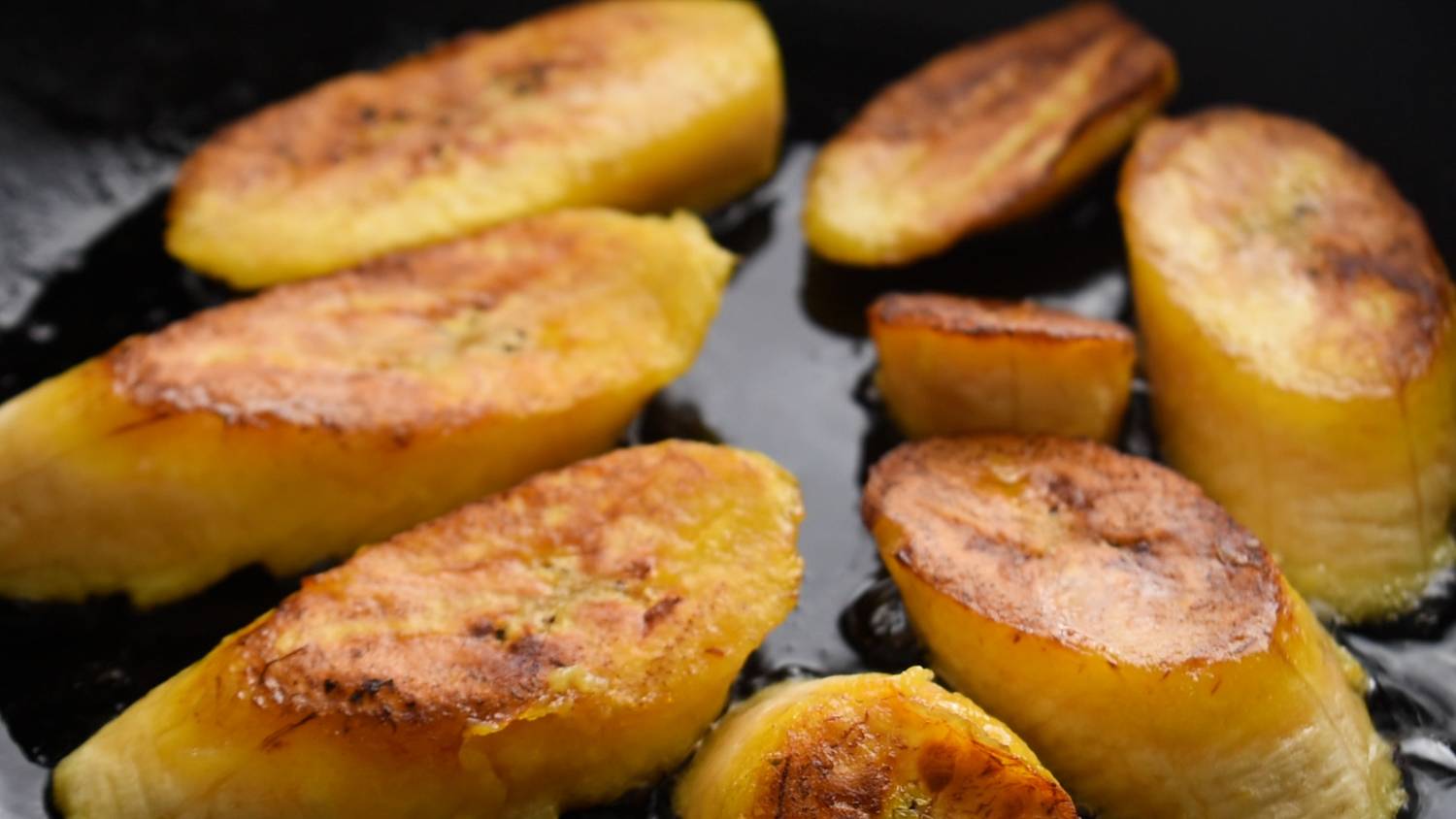 Ripe plantain slices are pan-fried until golden brown with crispy edges, creating a warm and appetizing scene. The surface is shiny.