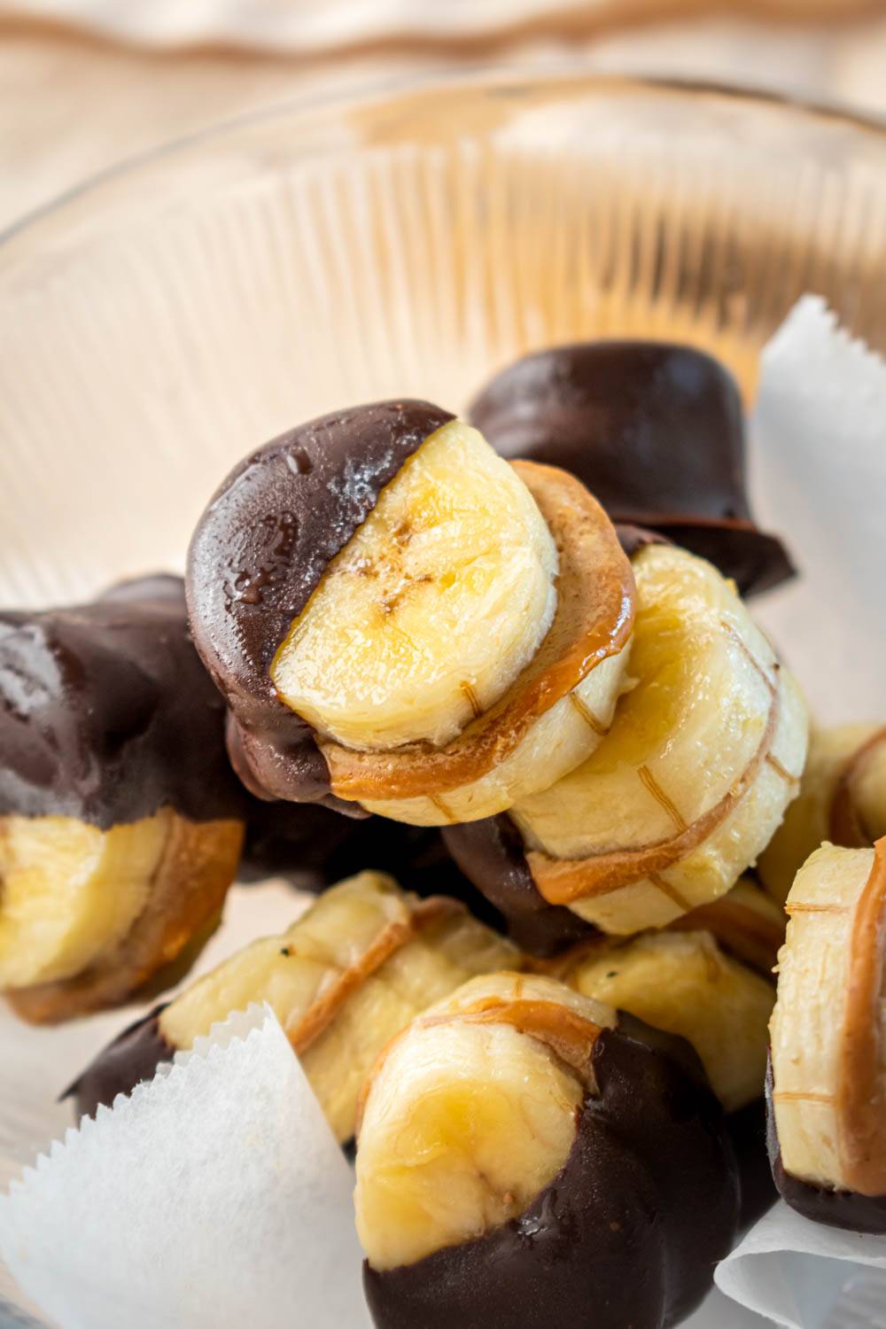 A close-up of sliced bananas dipped in chocolate, arranged in a glass bowl with a white paper lining.