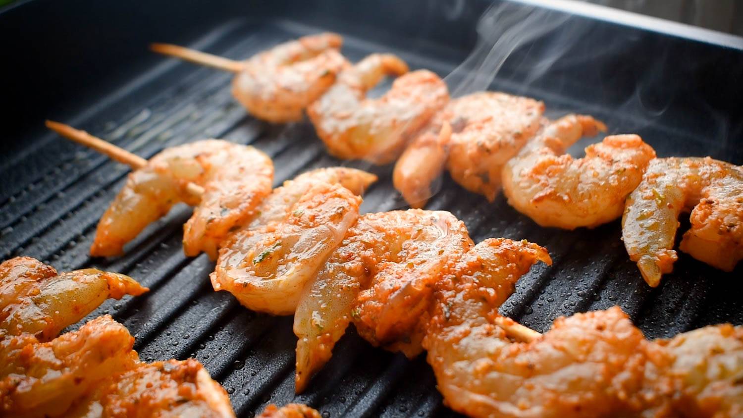 Grilled shrimp skewers sizzling on a hot grill, coated in spices, with steam rising in the background.