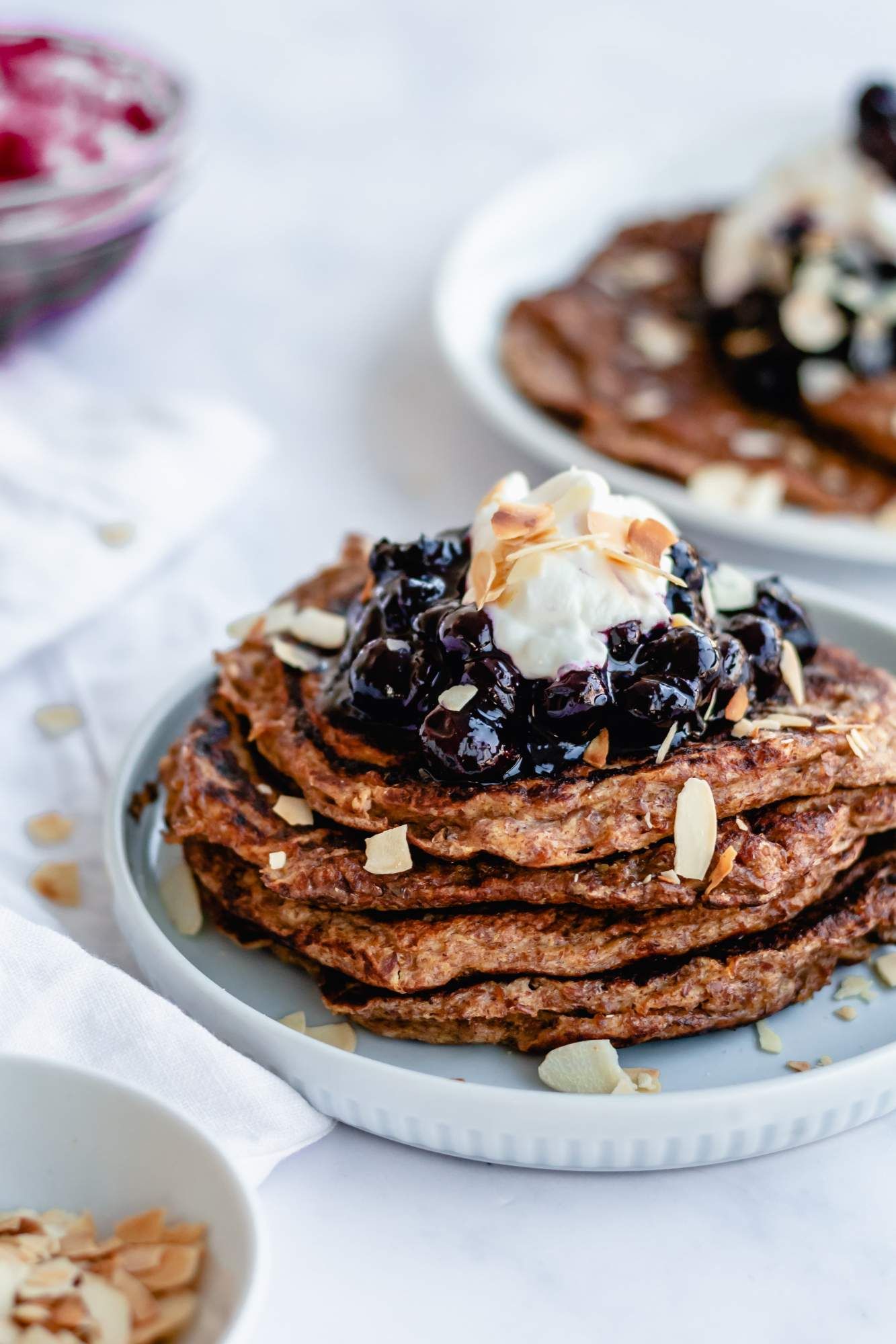 Flax and Greek yogurt pancakes in a stack with blueberries, yogurt, and almonds.