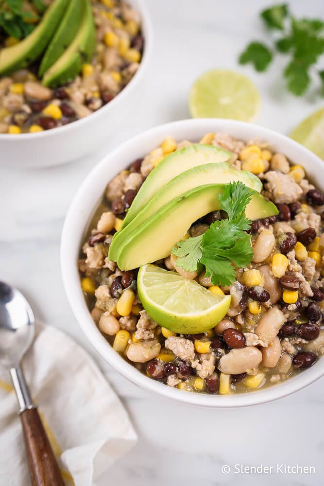 Ground turkey  green chili with sliced avocado, cilantro, and limes in two bowls.