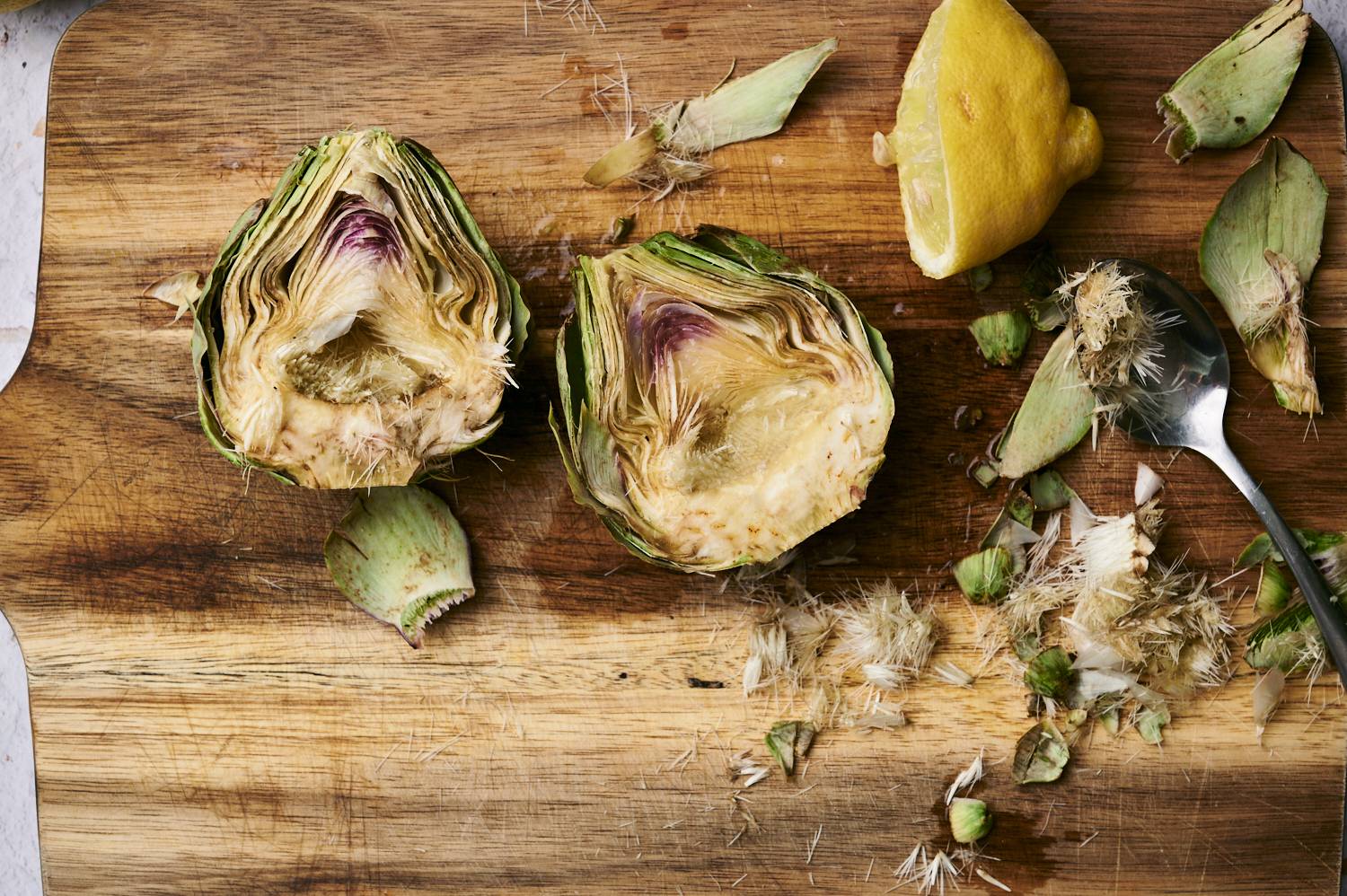 Artichokes being prepped for the grill with the choke scooped out on a cutting board.
