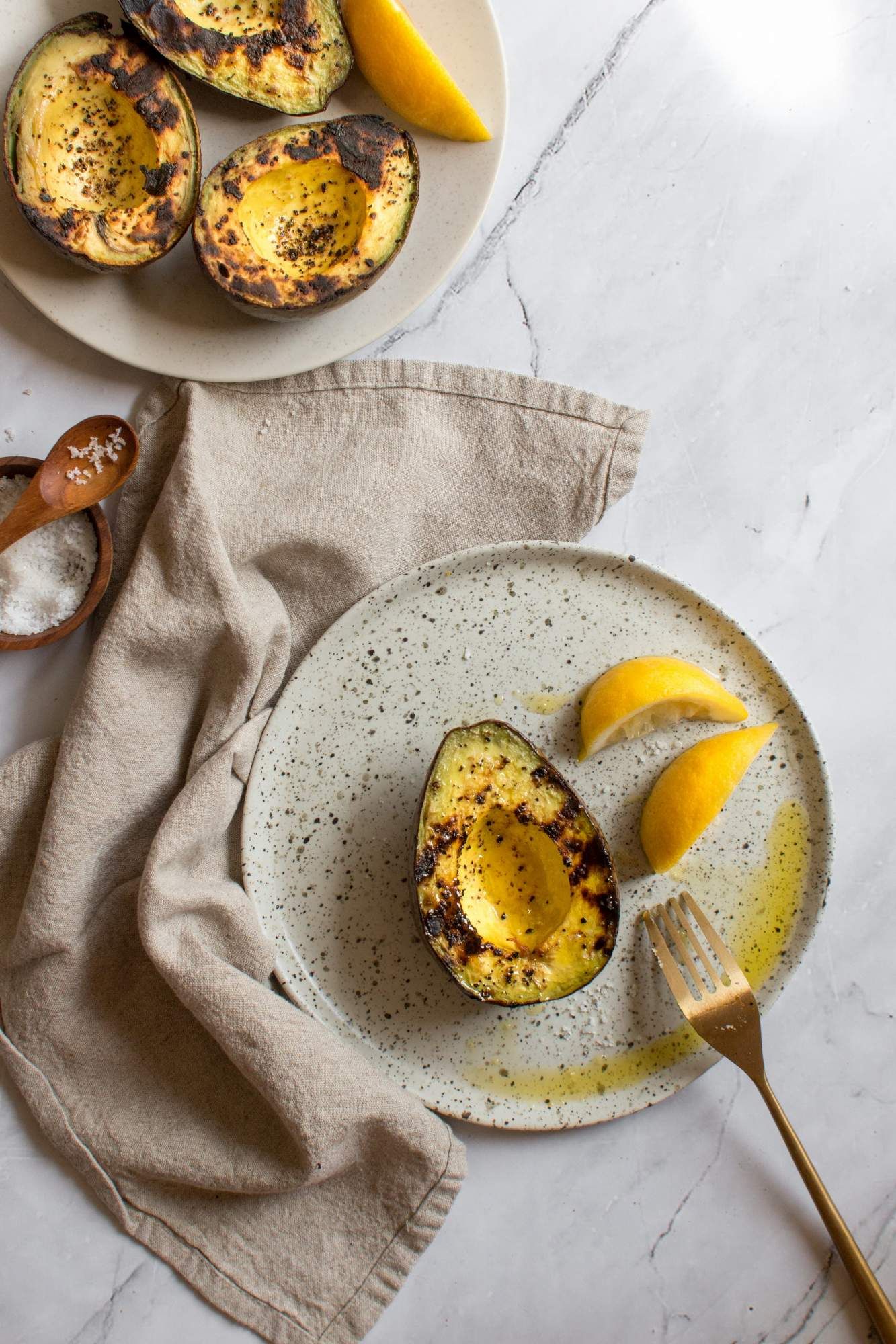 Grilling avocados sliced in half with grill marks topped with salt, pepper, and olive oil.