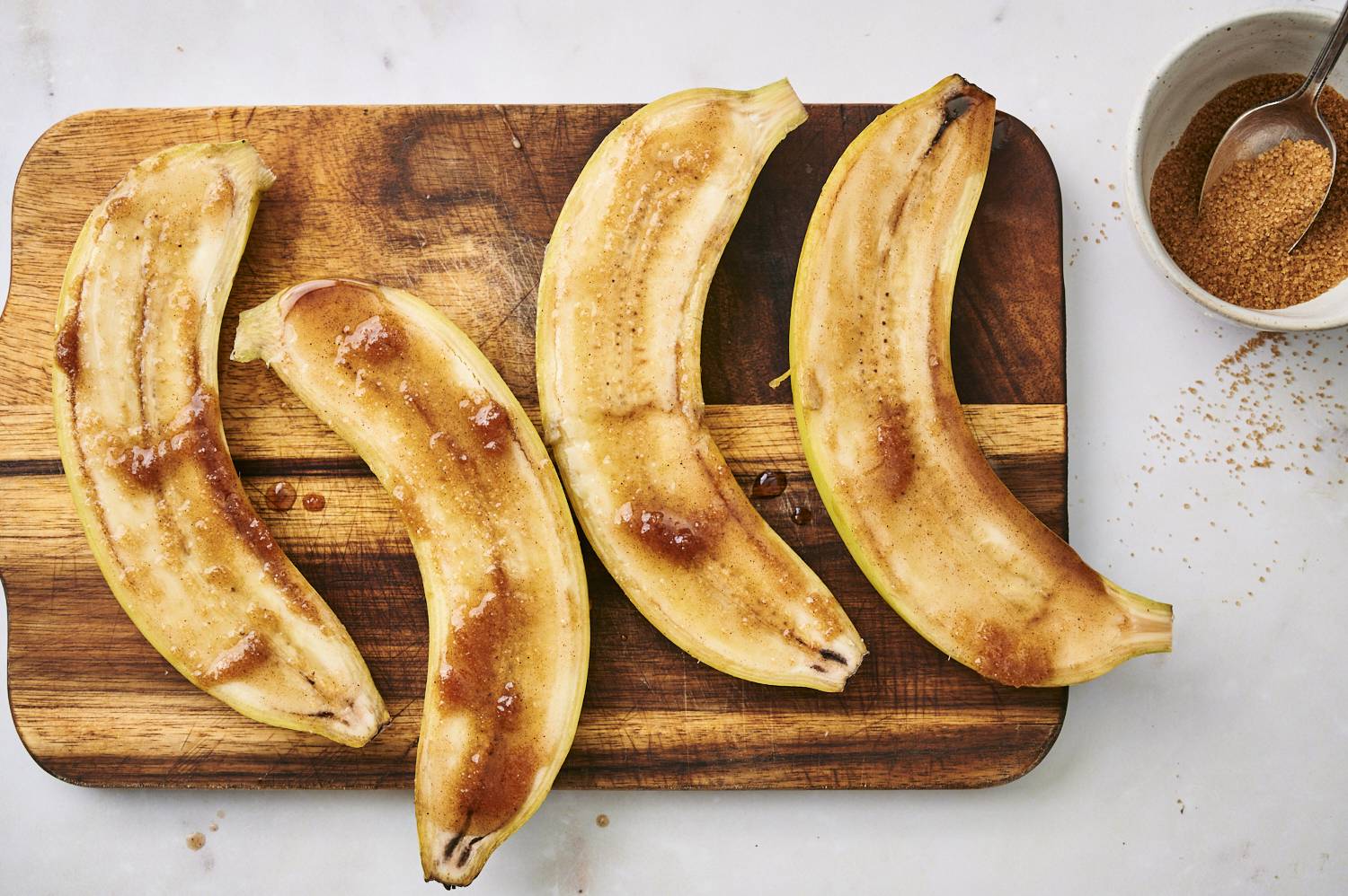 Sliced bananas with melted butter, brown sugar, and cinnamon on a wooden cutting board.