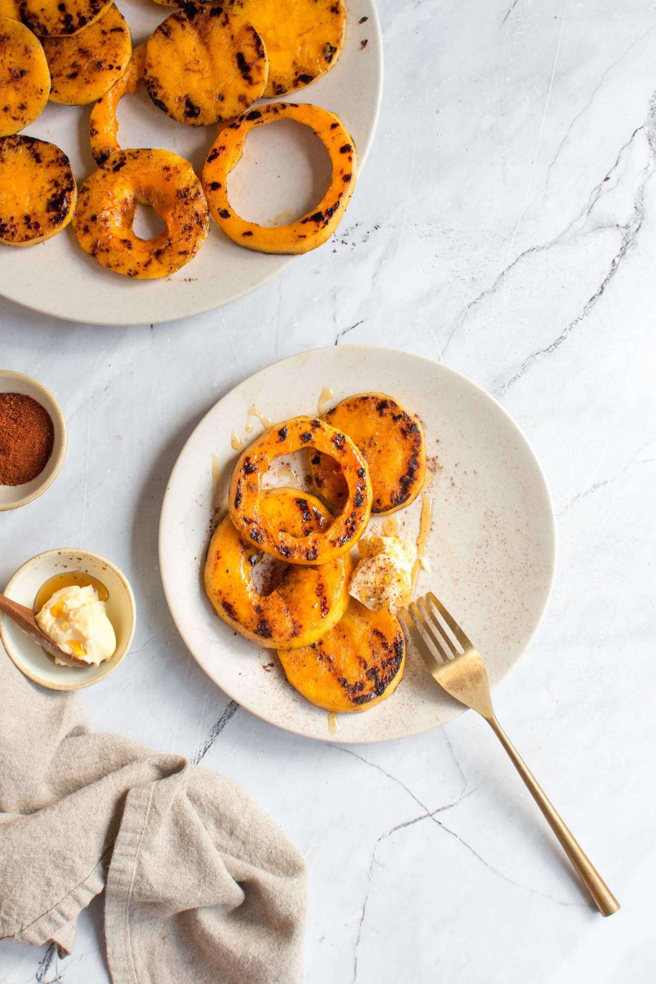 Butternut squash that has been grilled on a plate with a spice blend and butter on the side.