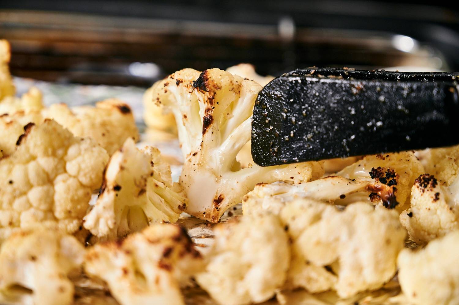 Cauliflower florets being cooked on a grill with tongs.