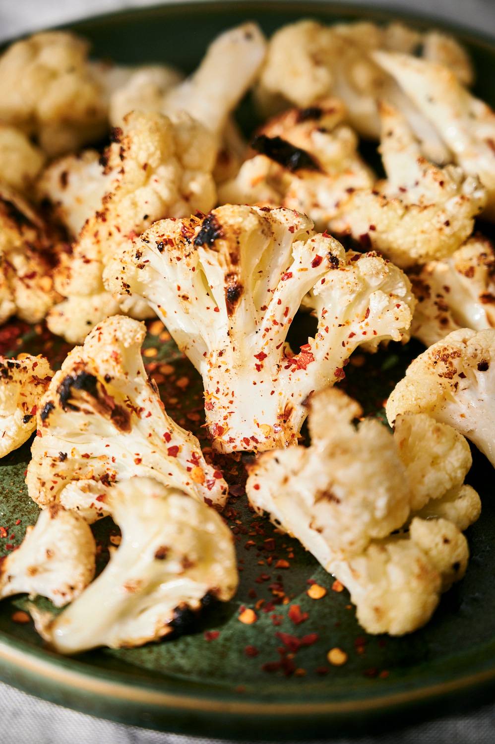 Crispy grilled cauliflower served on a plate with salt, pepper, and red pepper flakes.