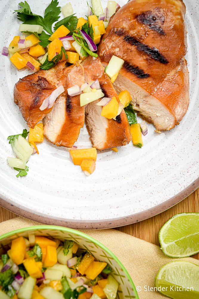 Grilled chicken with peach salsa on a plate with peach and cucumber salsa on the side.