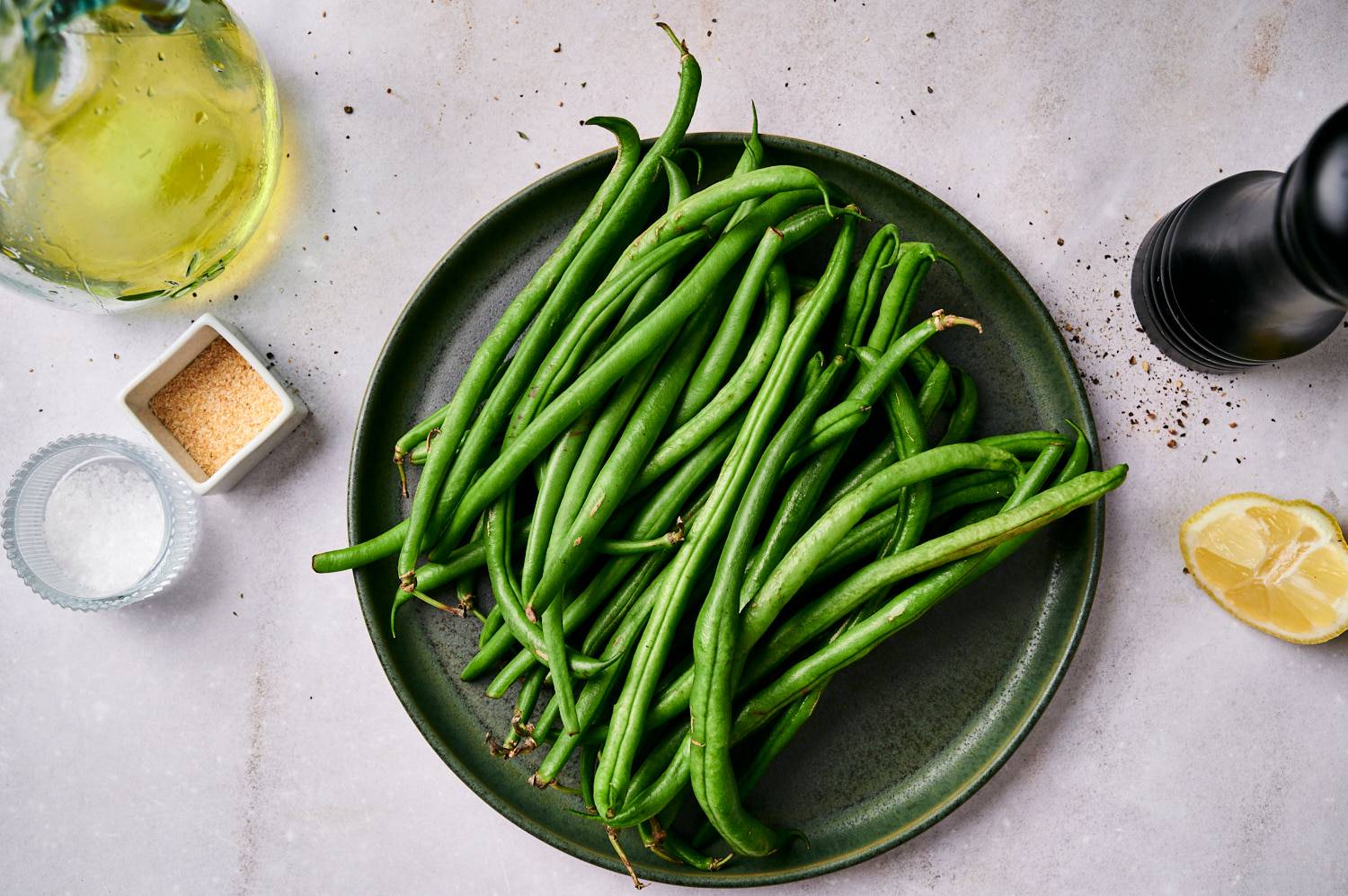 Ingredients for grilled green beans including fresh green beans, lemon, pepper, salt, and olive oil.