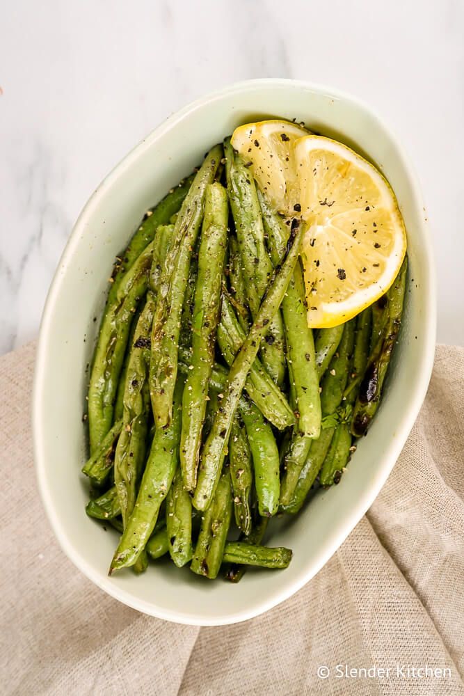 Grilled green beans with salt, pepper, and olive oil in a small dish.