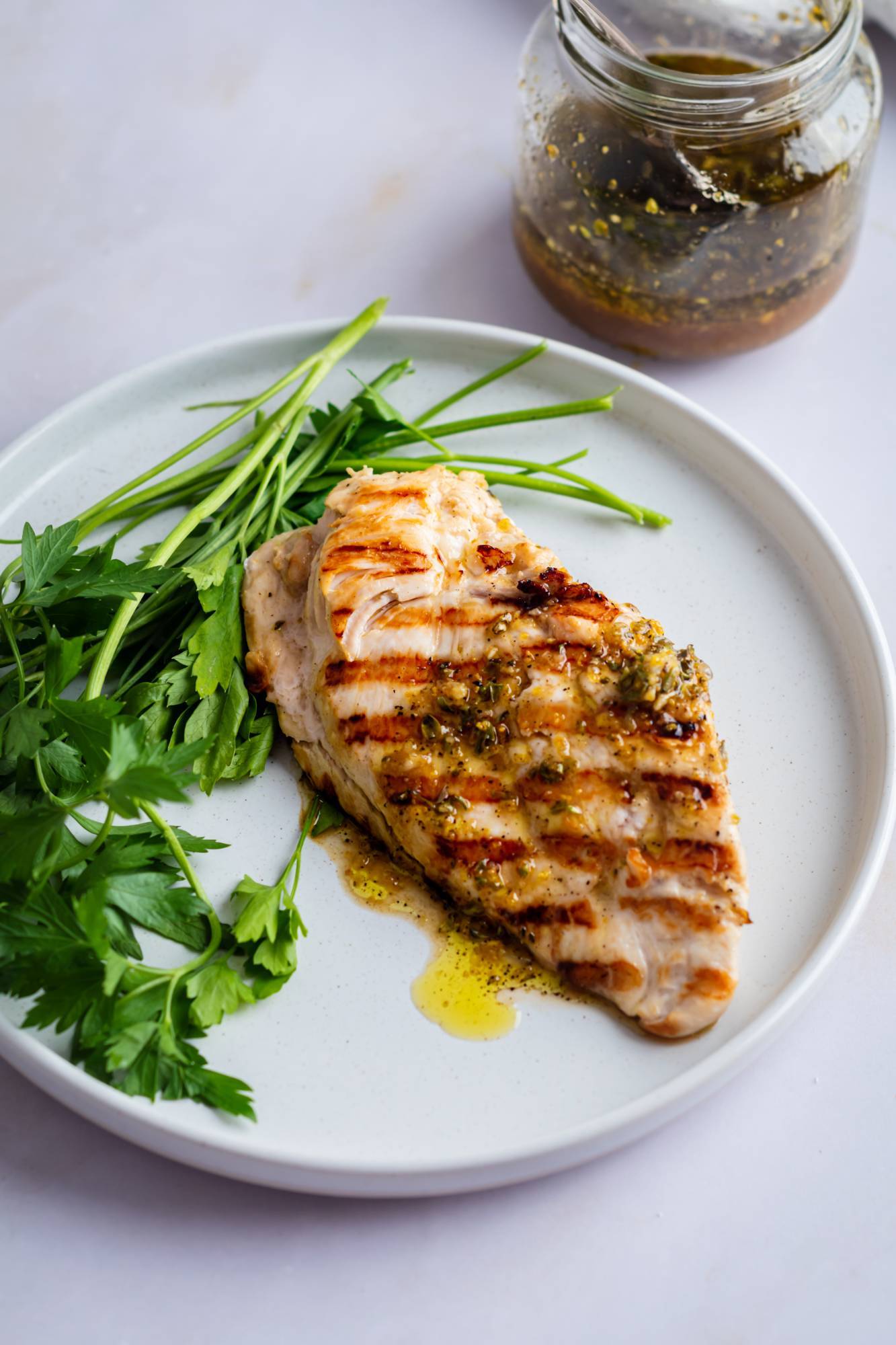 Lemon pepper grilled chicken with grill marks and lemon pepper sauce on a plate with parsley.