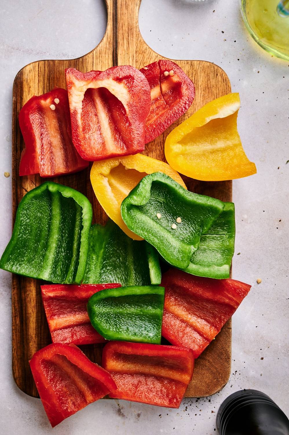 Sliced bell peppers on a cutting board with olive oil, salt, and black pepper.