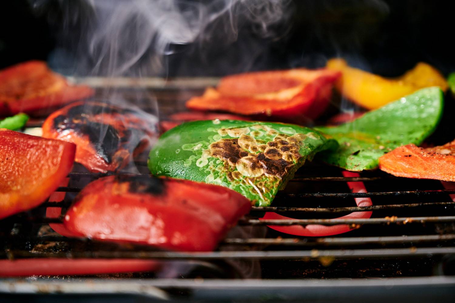 Bell peppers being cooked on a grill with char marks.
