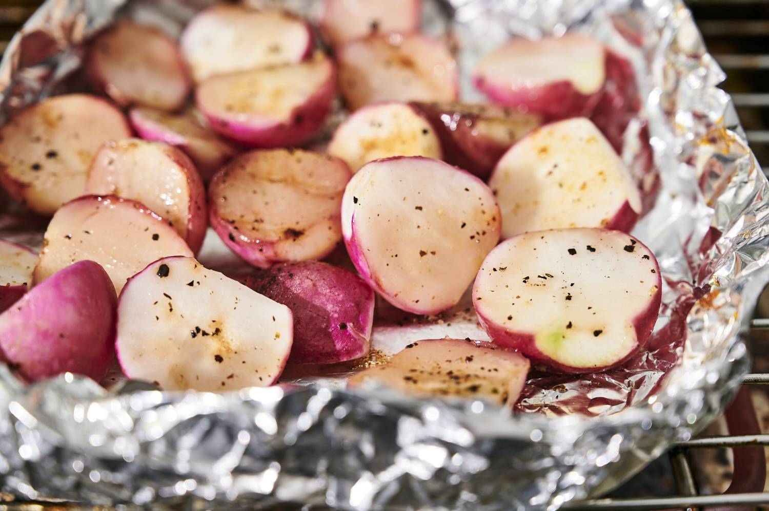 Radishes being grilled in a foil packet with salt and pepper.