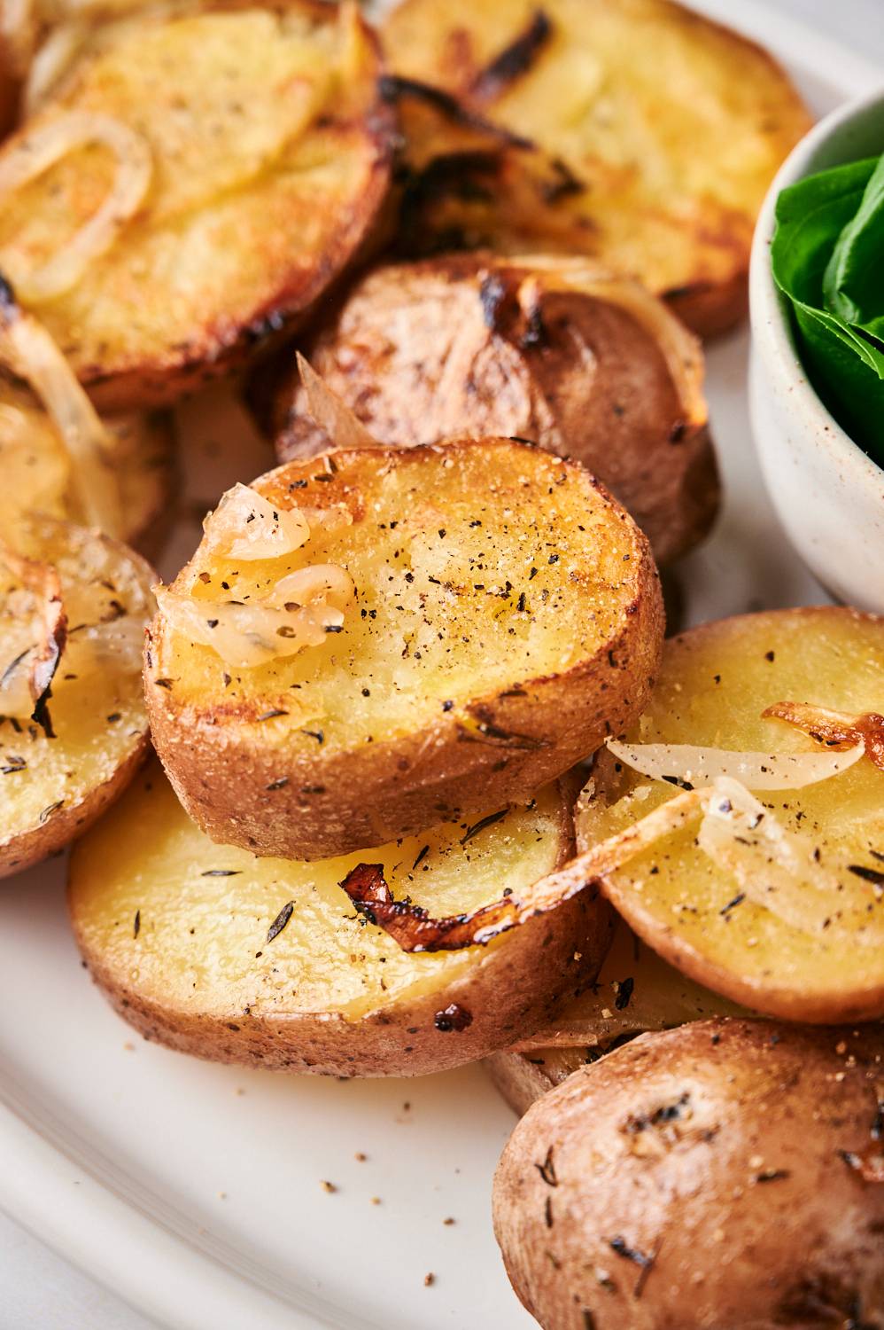Crispy grilled potatoes with sliced onions, rosemary, and olive oil on a white platter.