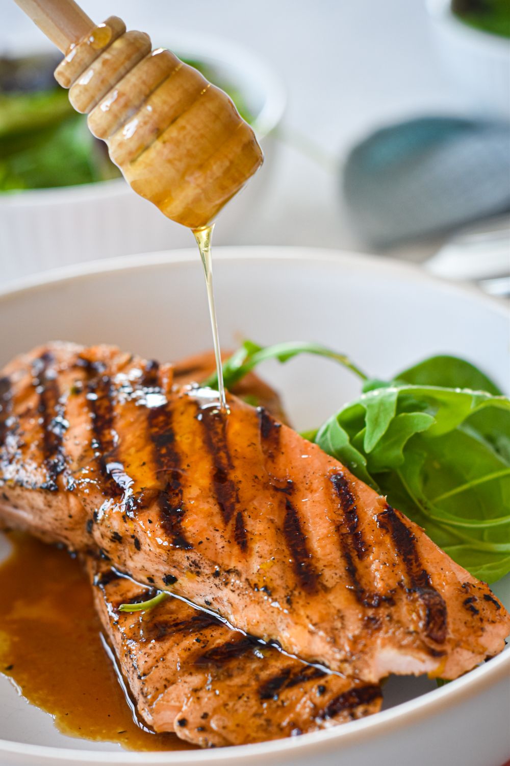 Grilled salmon with honey and lime on a plate with honey being drizzled on top.