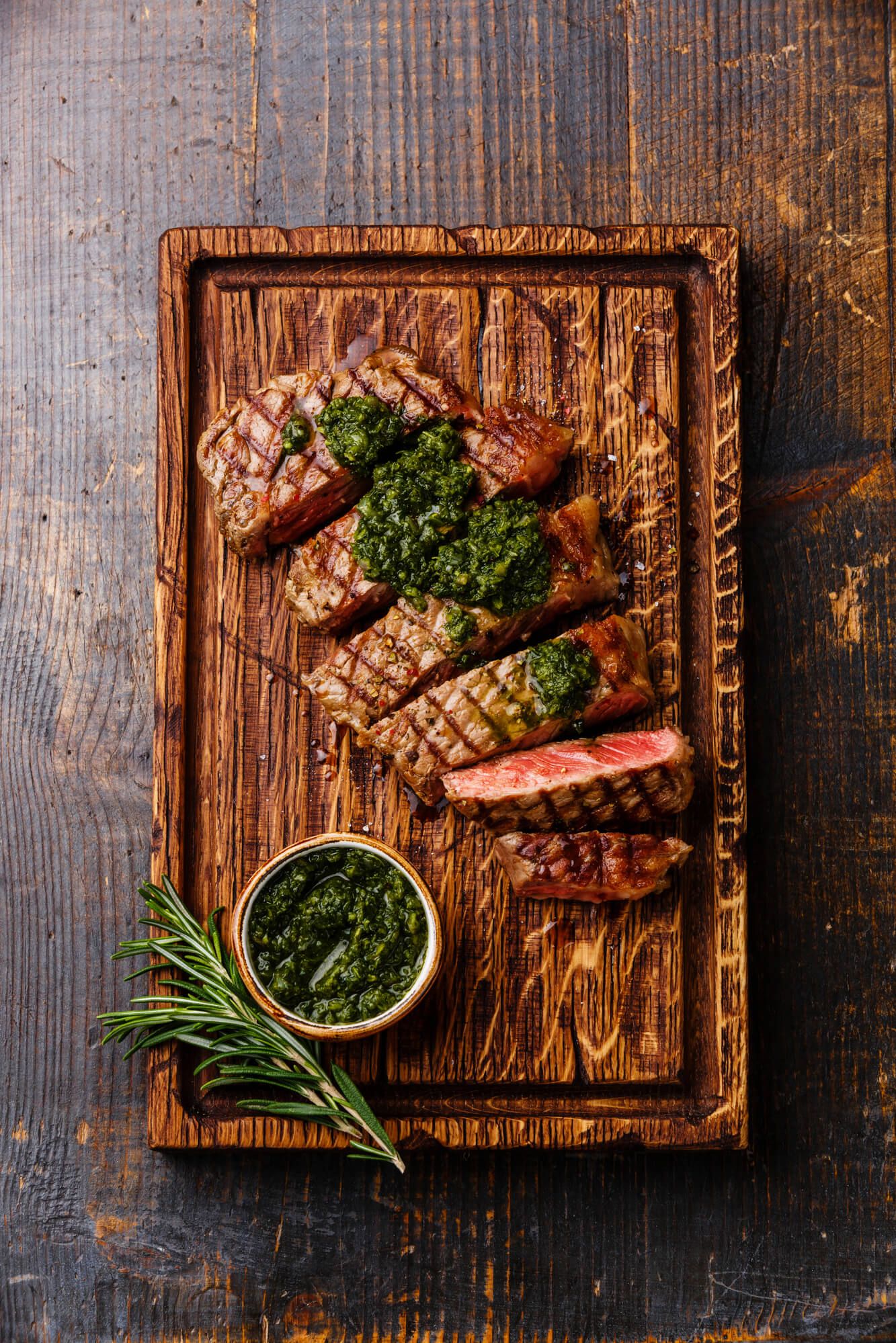 Grilled sirloin with chimichurri on a wooden cutting board.