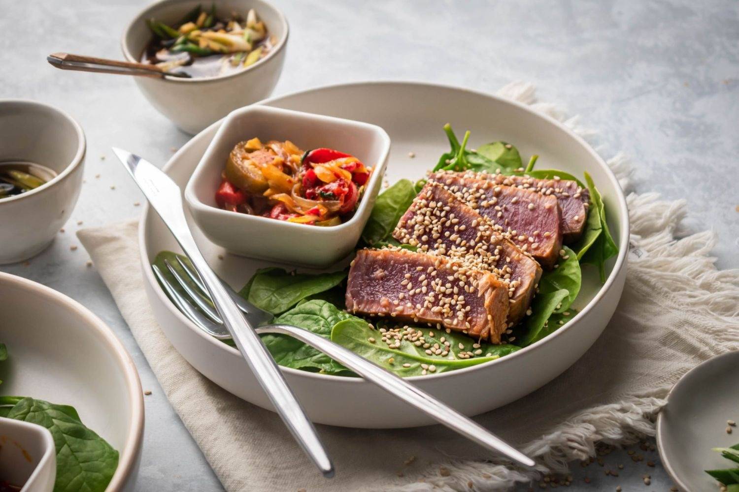 Grilled ahi tuna cooked rare and sliced on two plates with greens and a pepper relish.