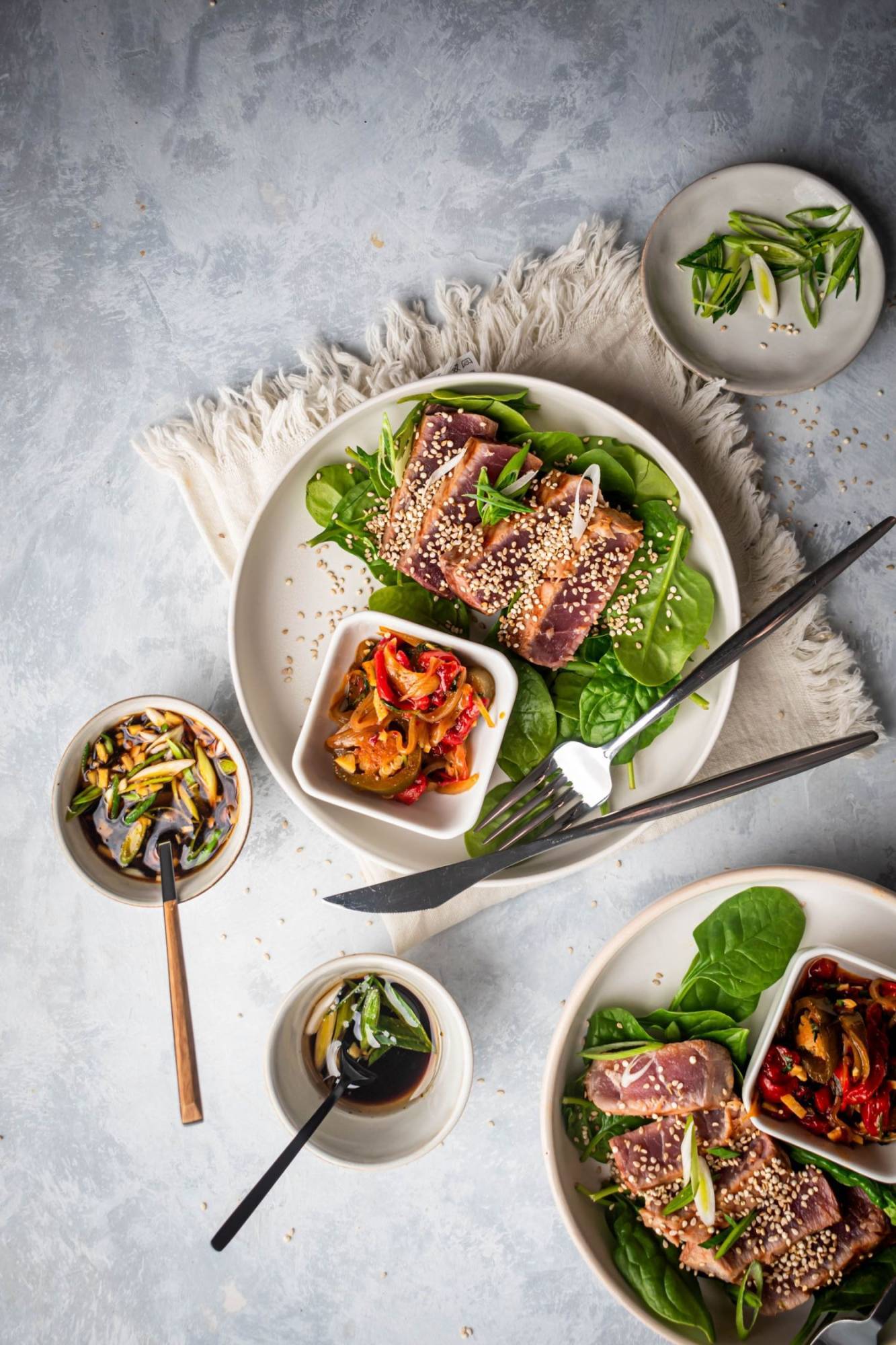 Grilled slice ahi tuna with sesame seeds, soy sauce, and green onions on two plates with greens.