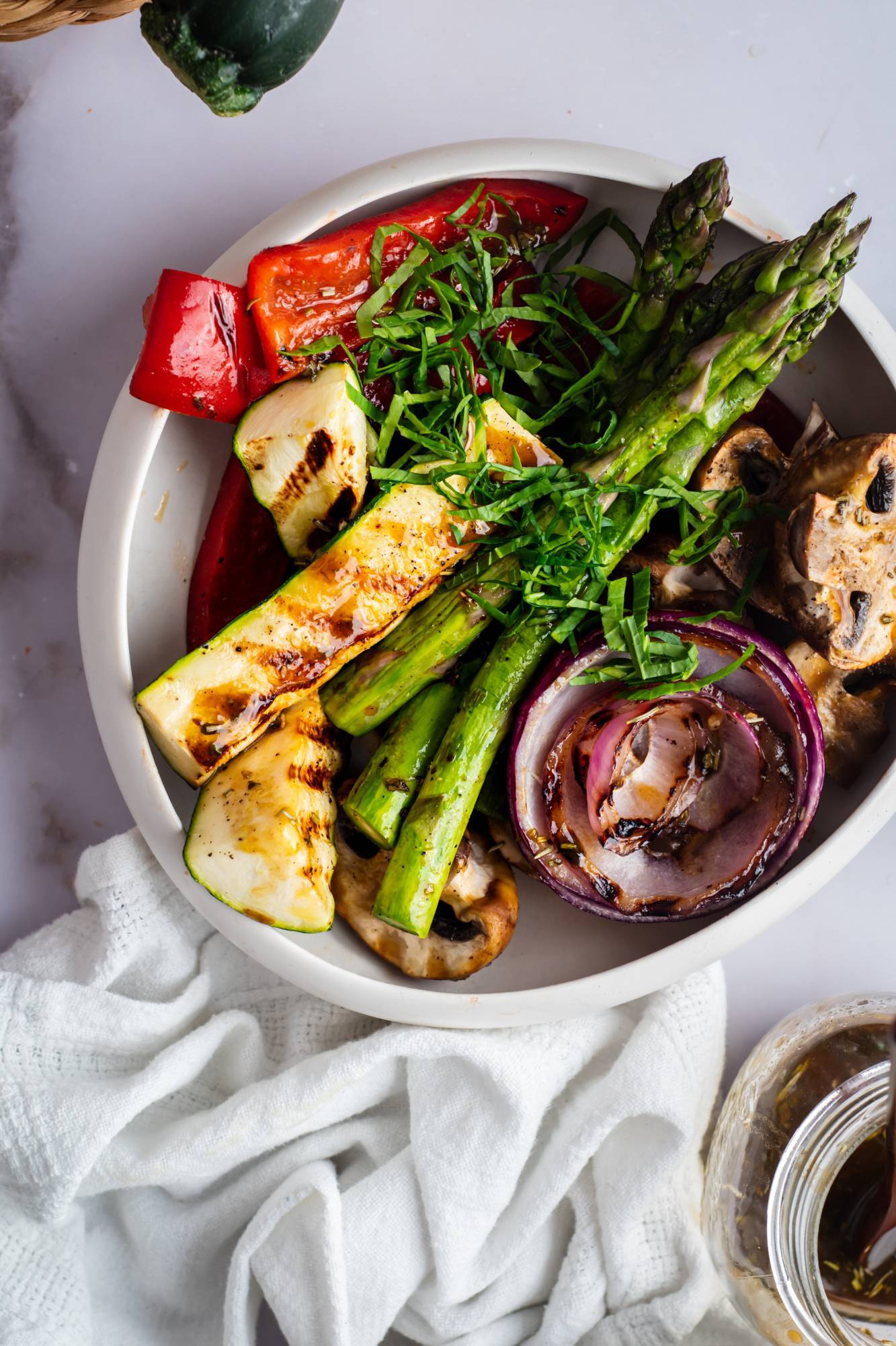 Grilled vegetables in a bowl with asparagus, zucchini, red onion, peppers, and mushrooms in balsamic marinade.