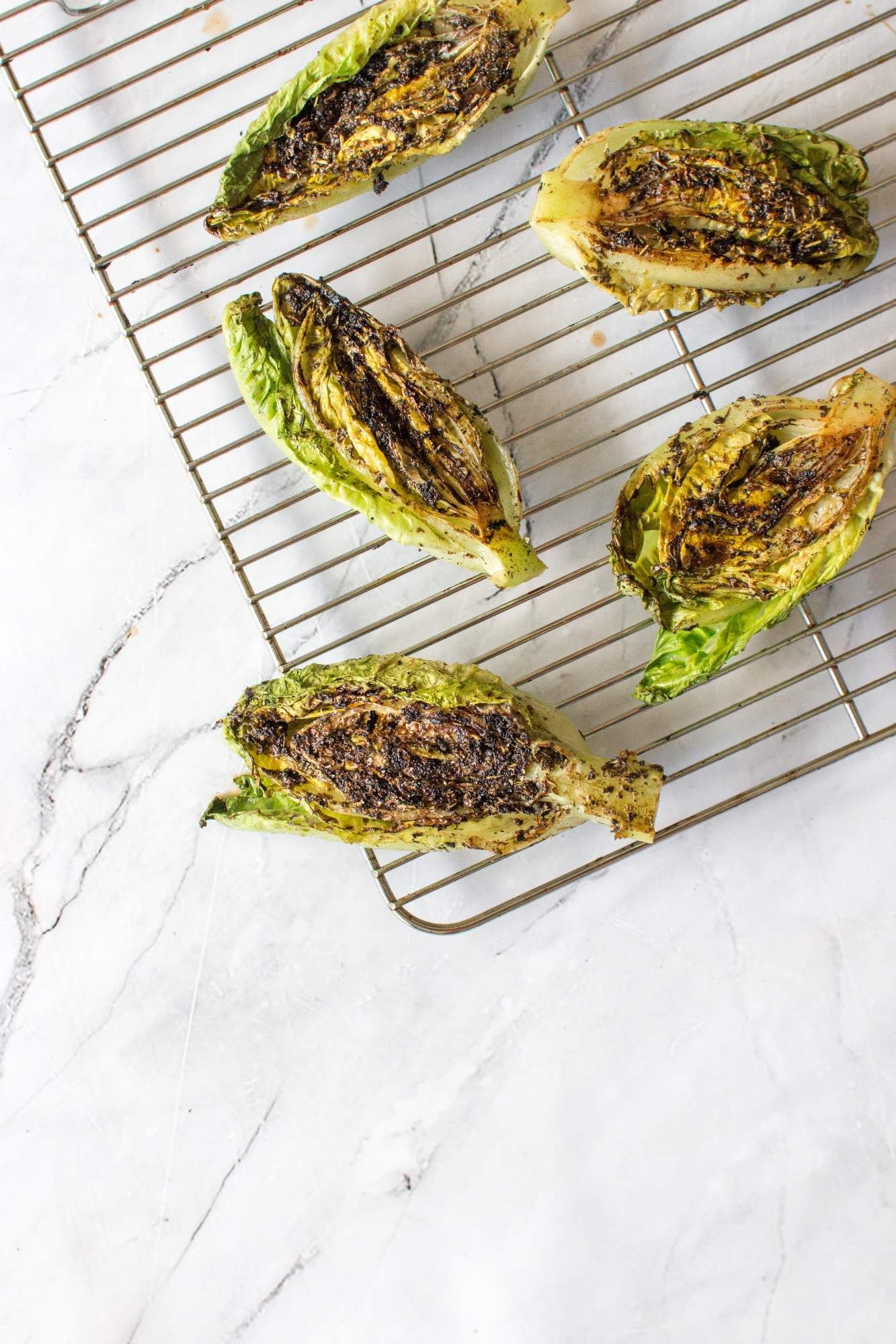 Grilled lettuce on a wire rack with grill marks, olive oil, salt,  and pepper.