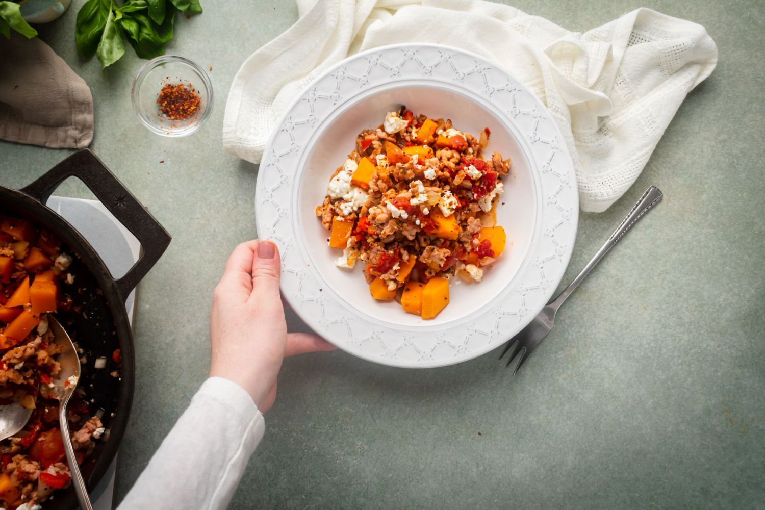 Butternut squash and turkey skillet with feta cheese served with red pepper flakes and basil.