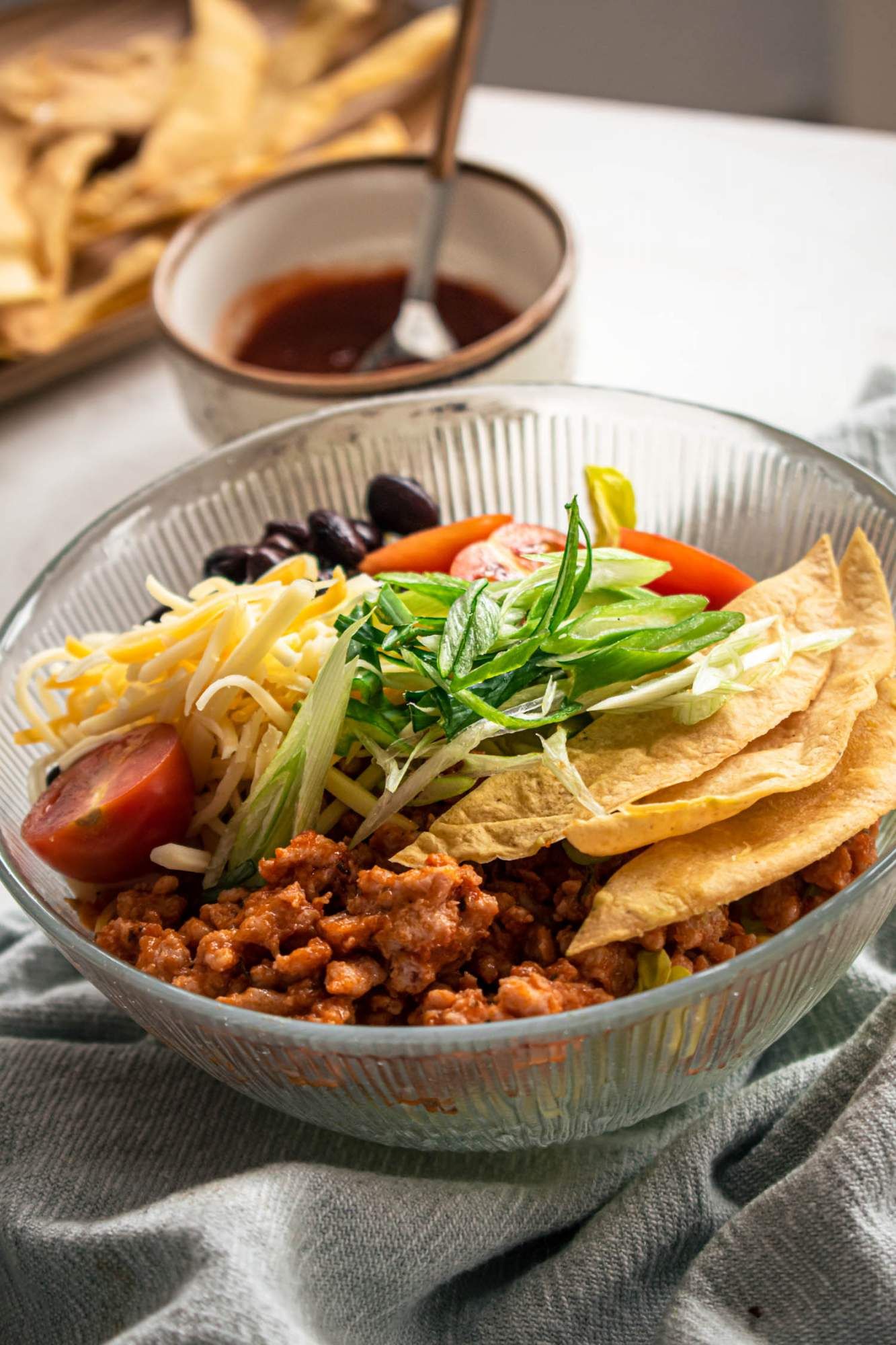 Salad with turkey taco meat, black beans, tomatoes, green onions, romaine lettuce, and shredded cheese in a glass bowl with dressing on the side.